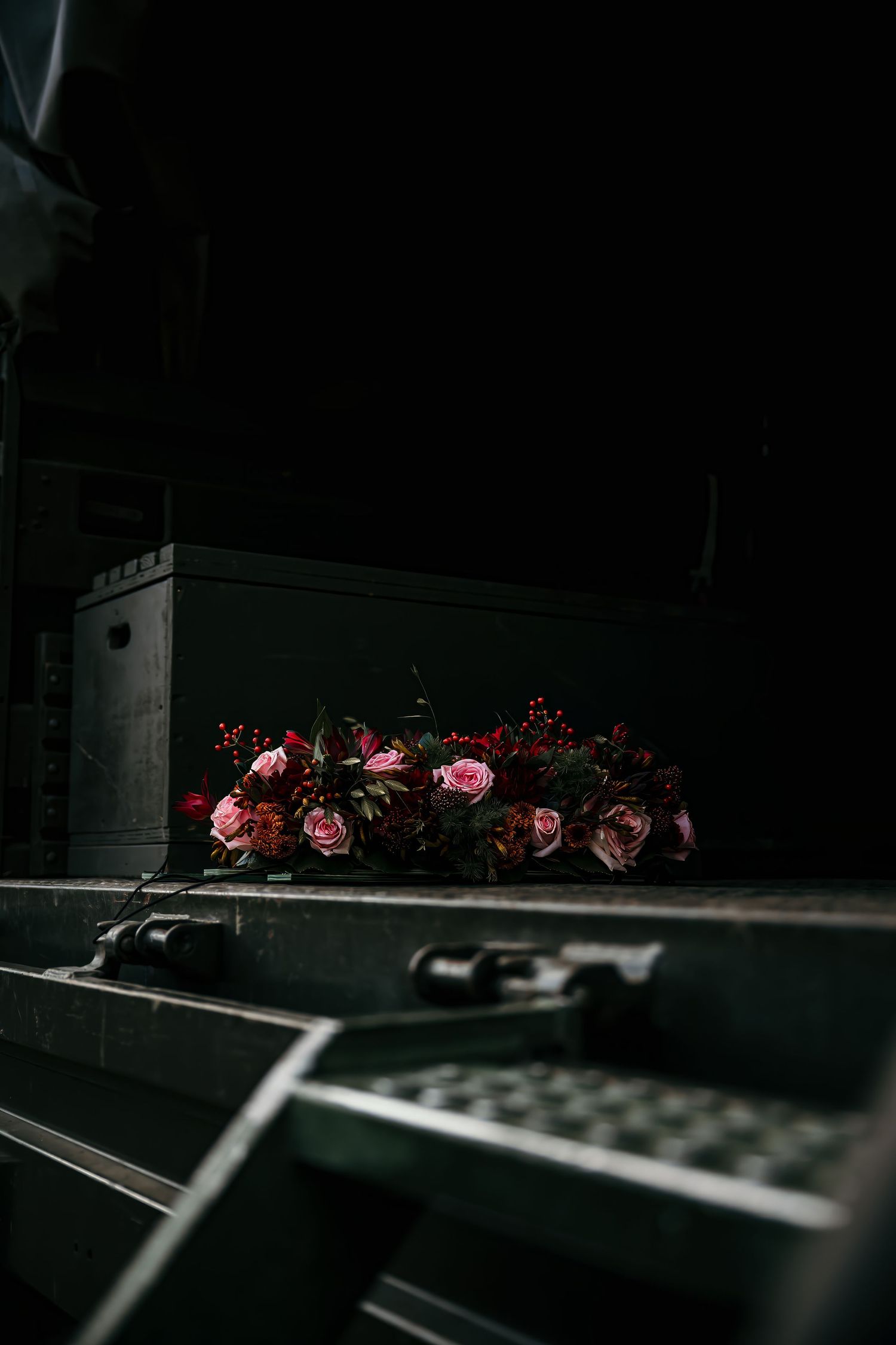 Pink roses lay scattered across a dark surface creating a moody and dramatic still life composition.