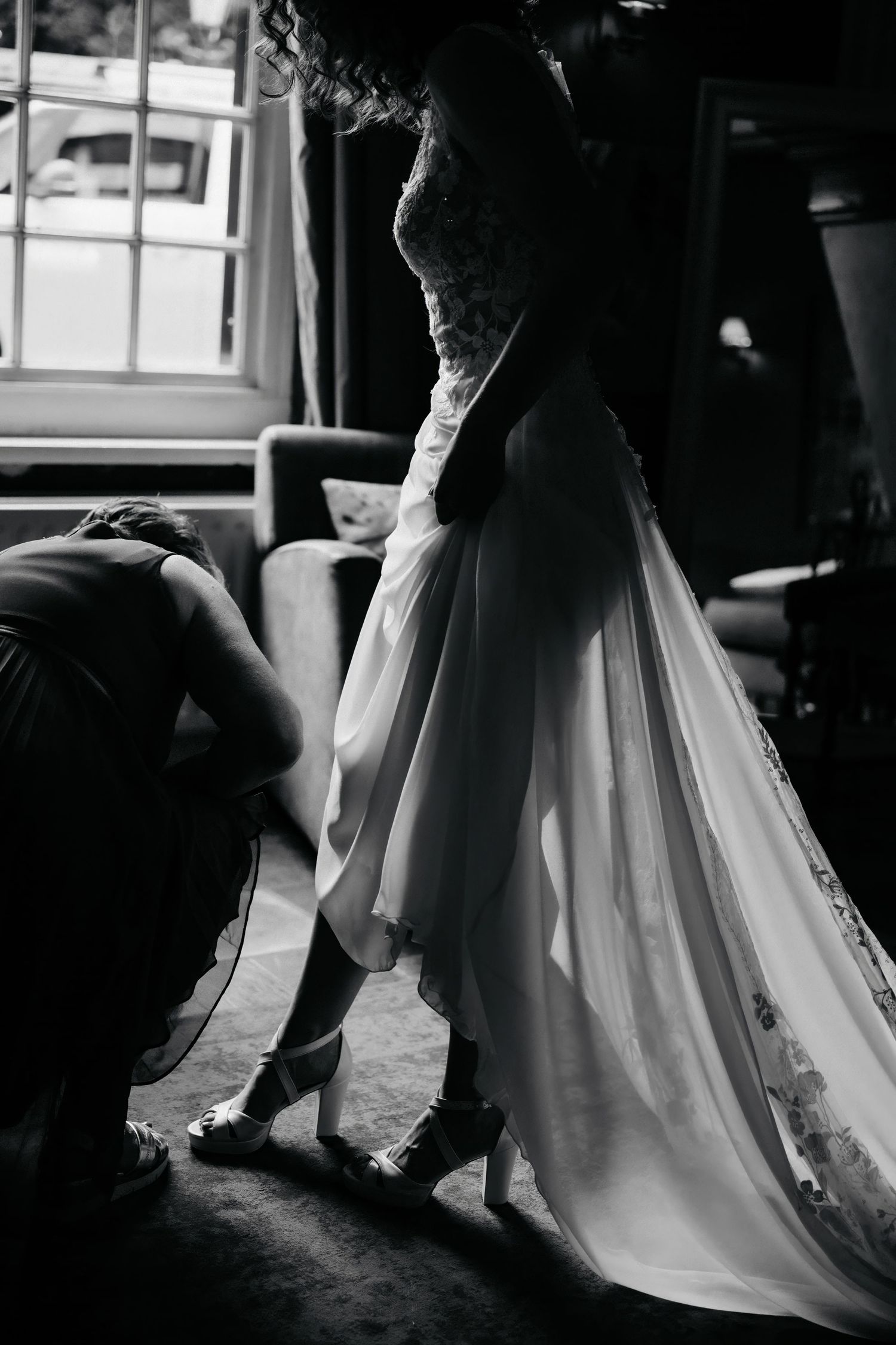 Close-up black and white shot of a wedding dress being adjusted in dramatic lighting.