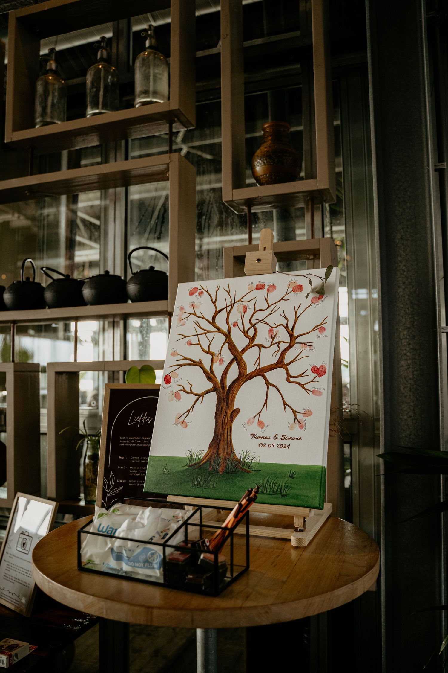 A wedding guestbook alternative featuring a painted tree on canvas displayed on a wooden table with bottles.