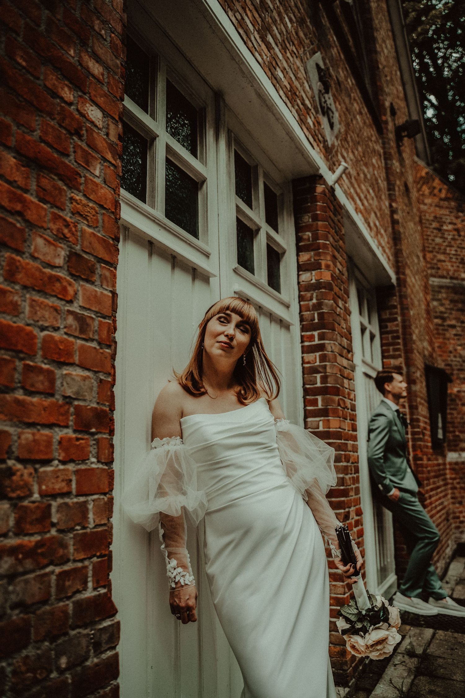 Wedding dress against rustic brick wall with white trim windows.