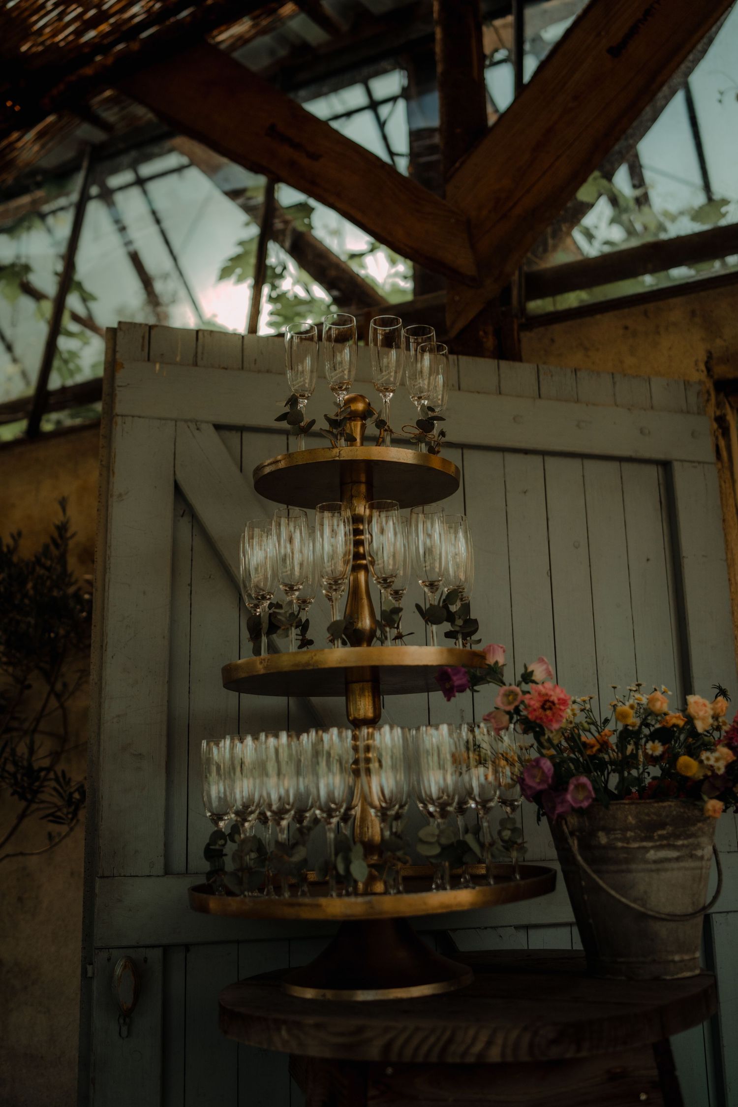 Vintage wooden tiered display stand with champagne glasses and floral decorations against a rustic wall.