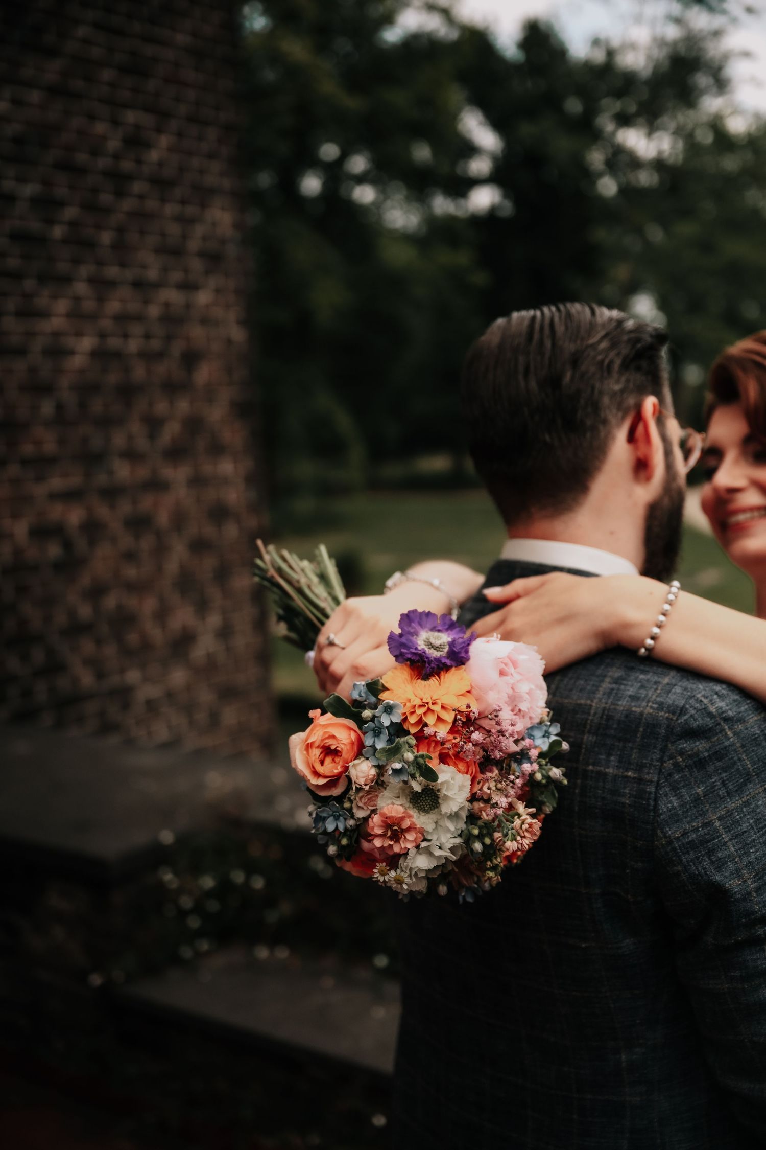 Colorful wedding bouquet with pink and purple flowers against dark background.