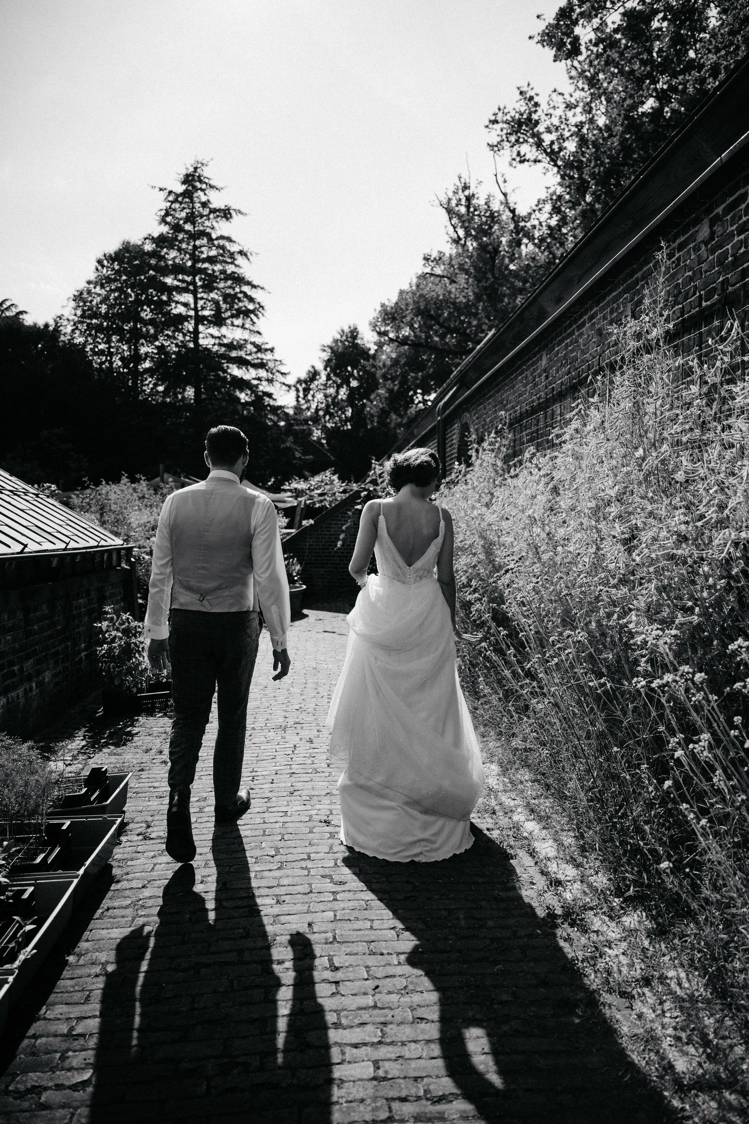 A couple walks down a brick path surrounded by garden walls on their wedding day.