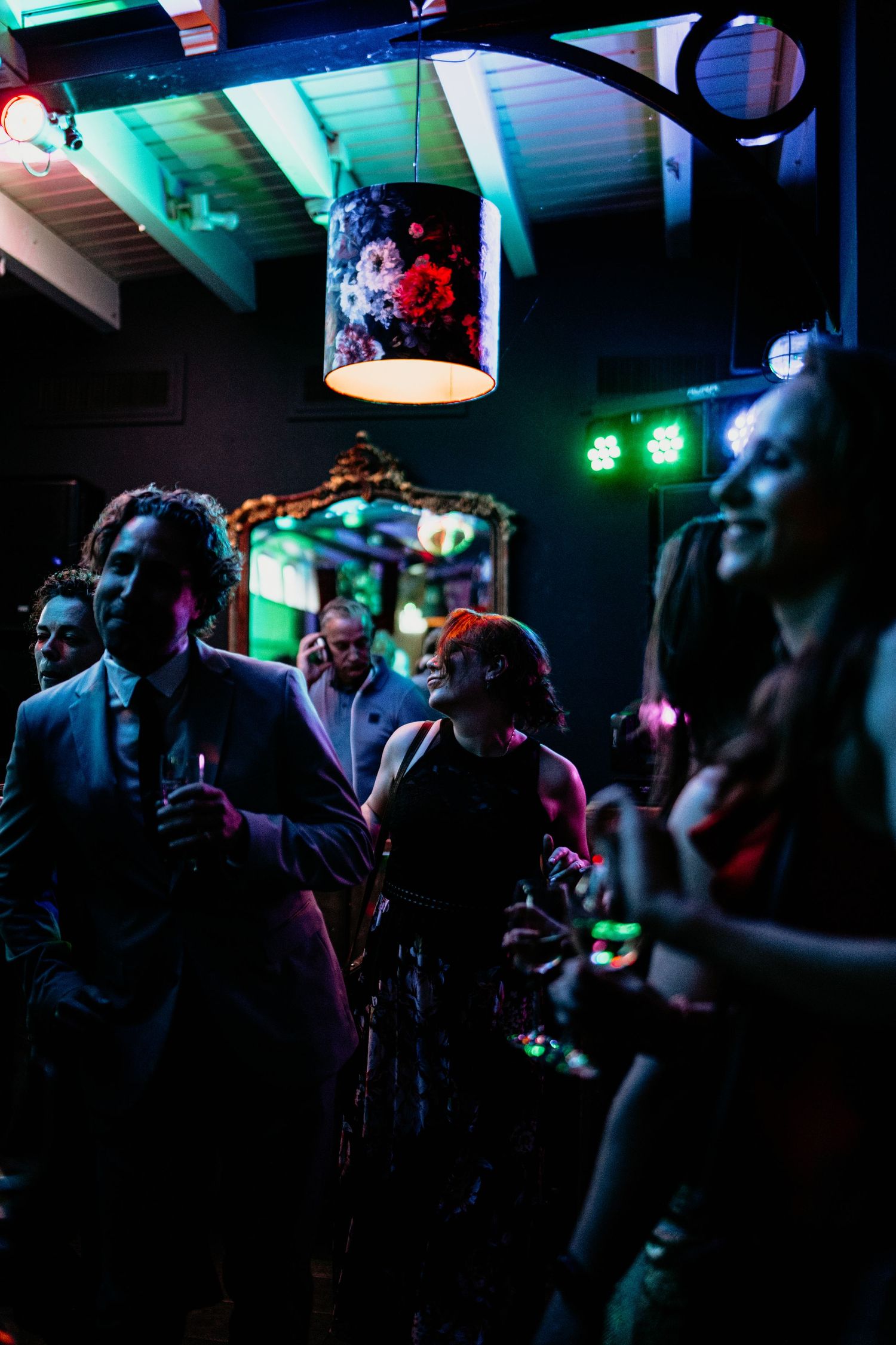 A dimly lit dance floor with colorful lights and party guests celebrating at a wedding reception.