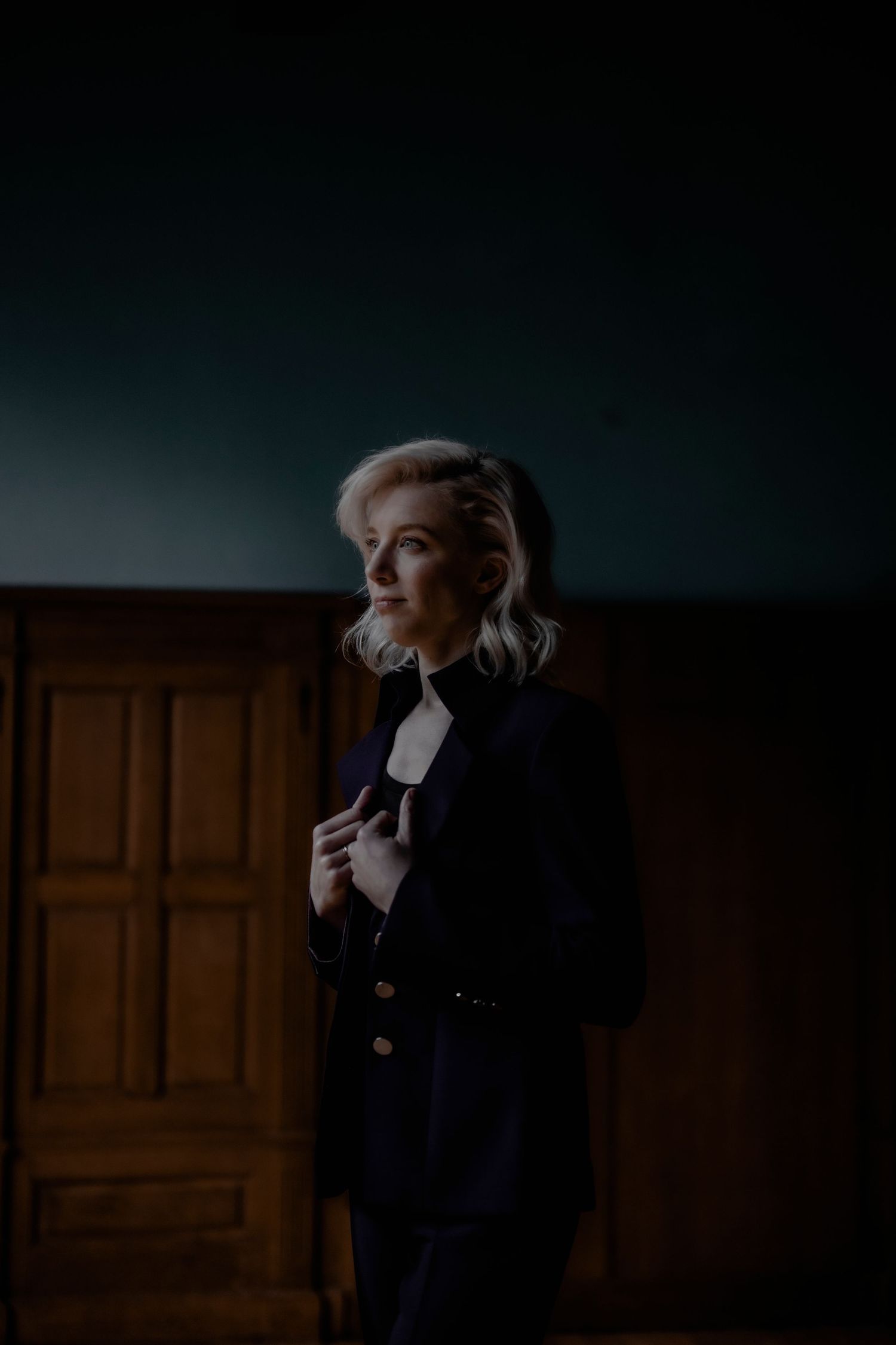 A series of moody dark portraits showing someone in a navy suit against a wooden door in dramatic lighting.