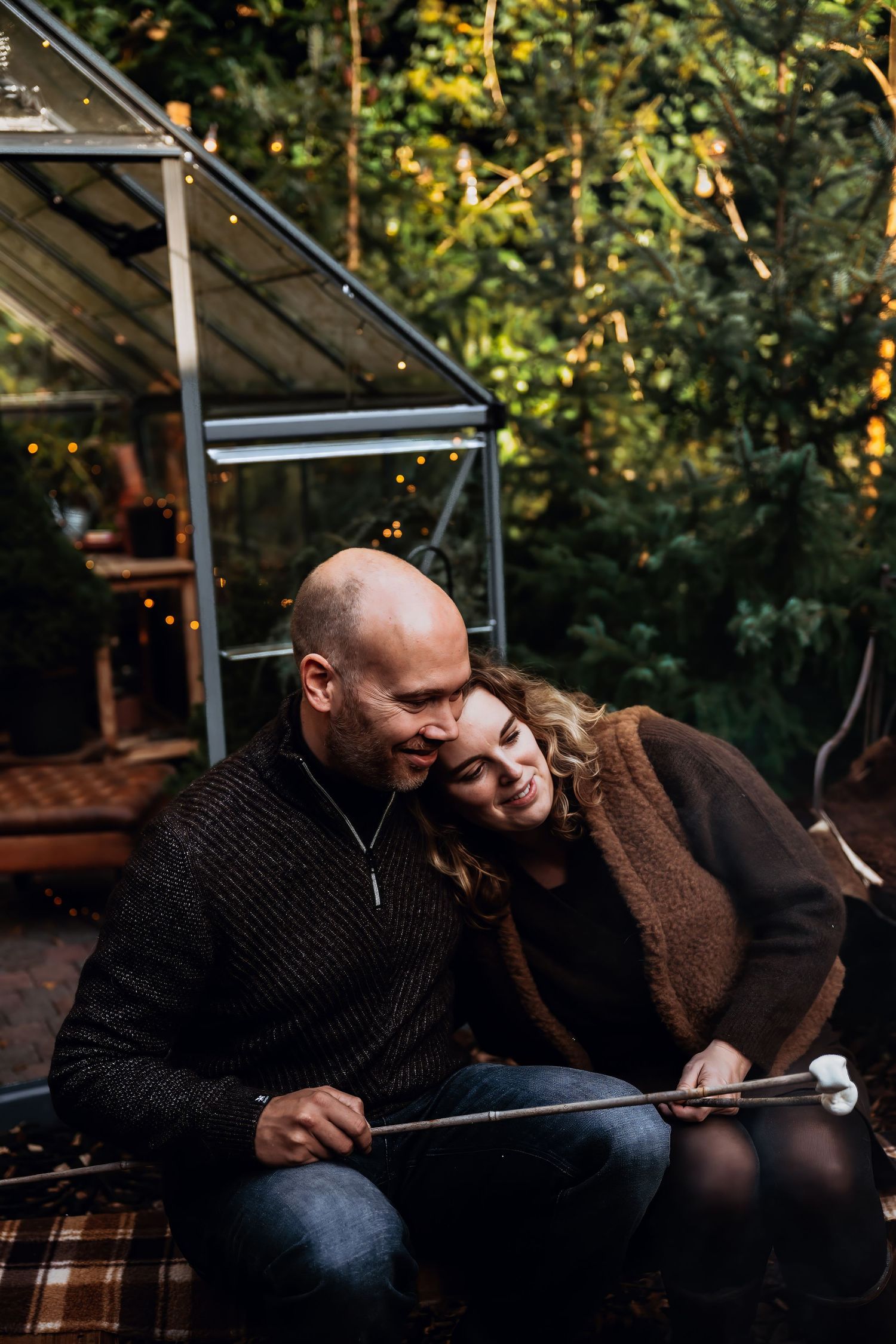 A cozy outdoor scene with a couple relaxing together near a greenhouse structure on a plaid blanket.