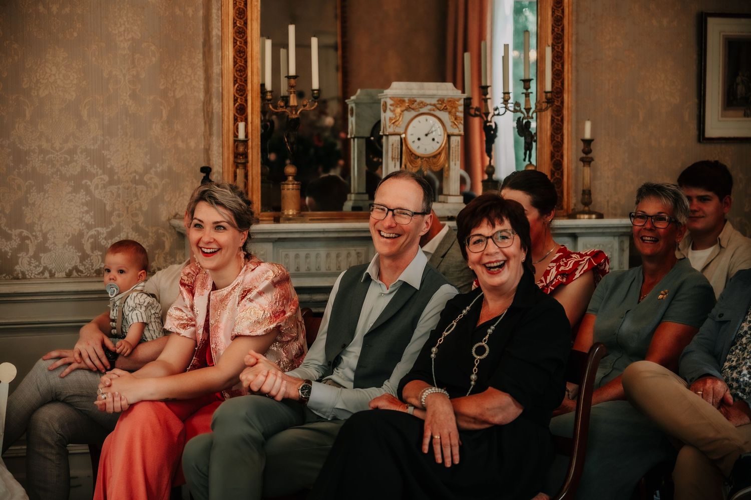 Wedding guests smile and laugh while seated in rows during a ceremony.