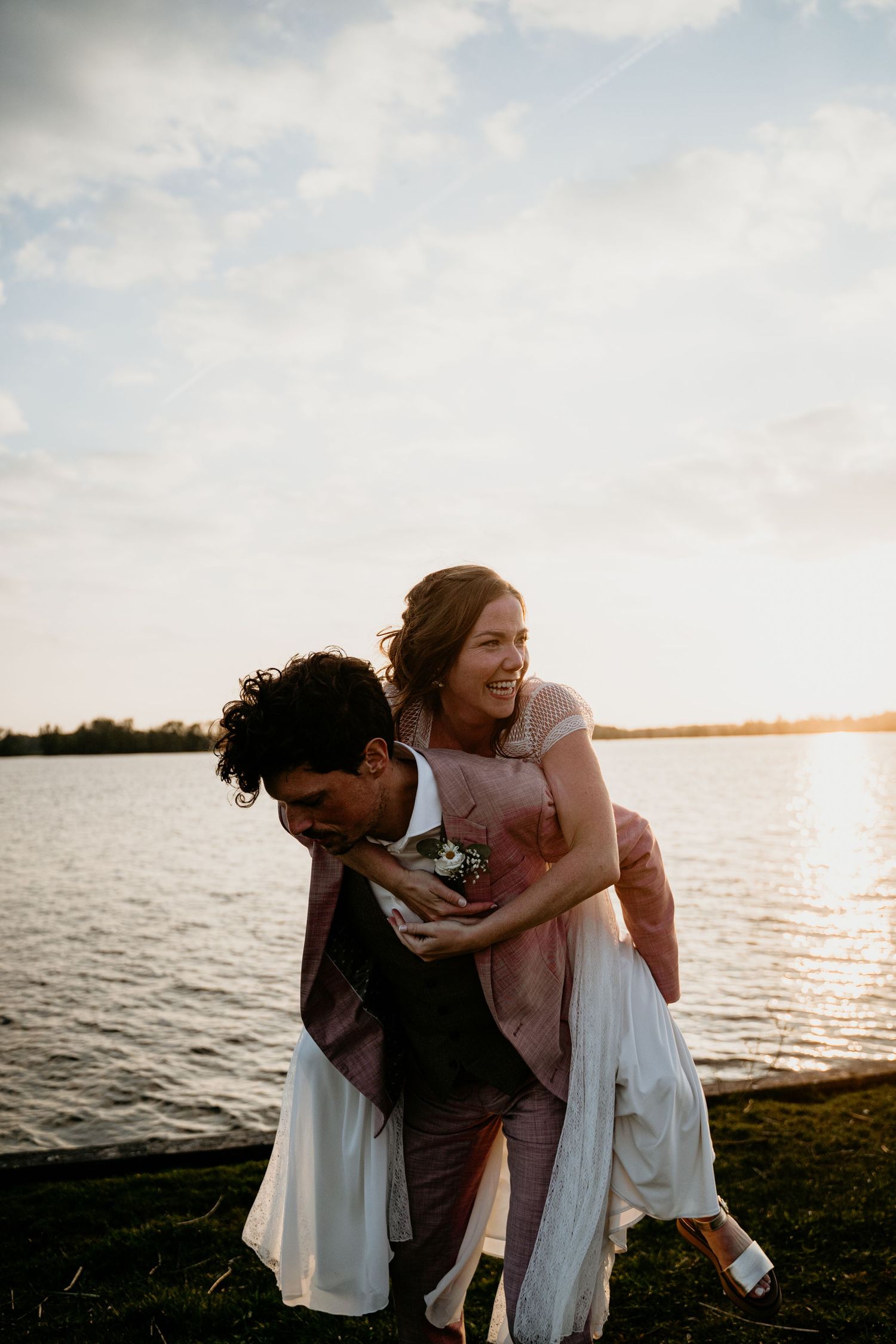 Wedding couple laughing together by the water during golden hour sunset.