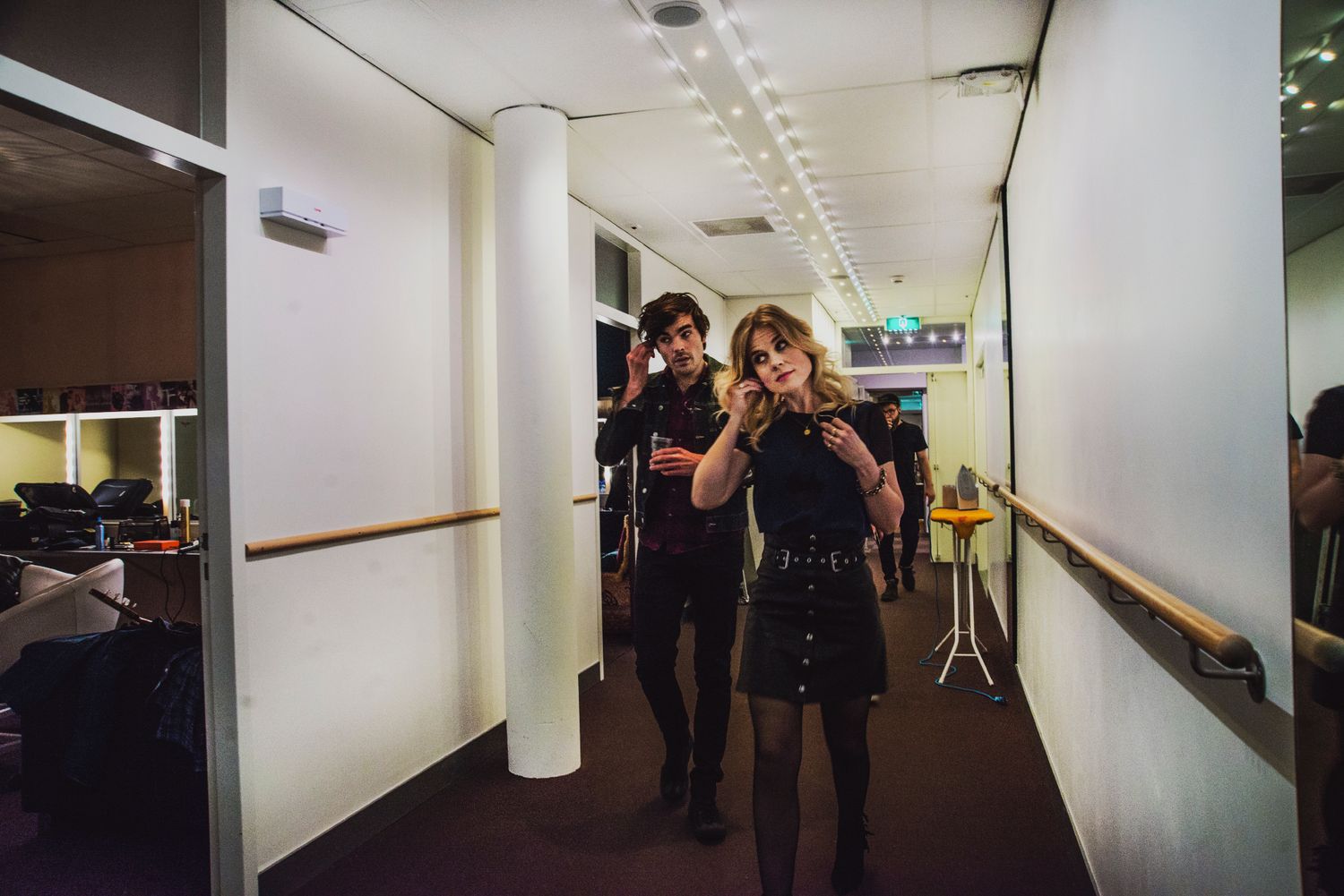 People walking through a dimly lit hallway with white walls and dark floors in an office or institutional building.