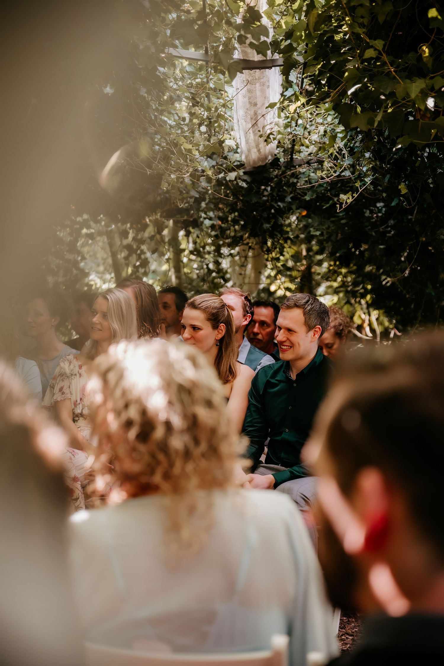 Wedding couple laughs together under a canopy of trees and twinkling lights during their celebration.