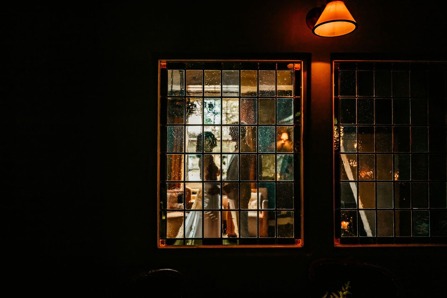 Illuminated windows at night showing silhouettes and warm lighting through multiple panes.