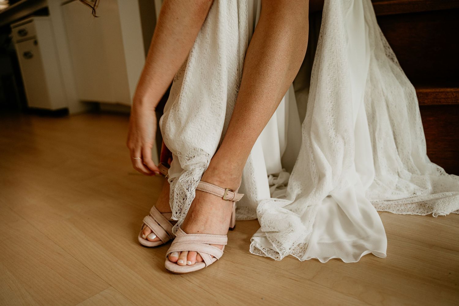 Close-up of white bridal shoes being fastened with delicate straps.
