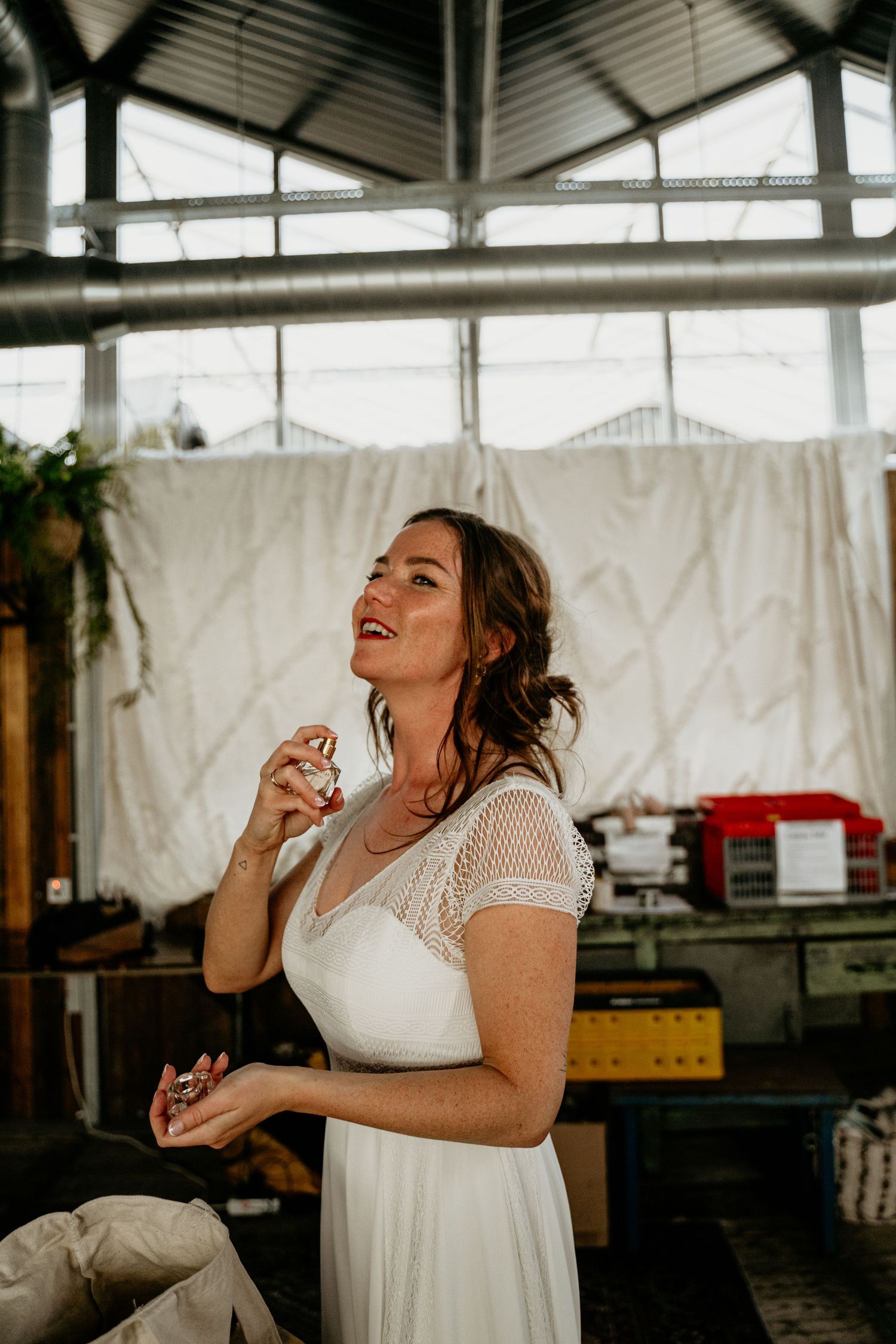 A bride in a lace-detailed white dress laughs joyfully in an industrial venue setting.