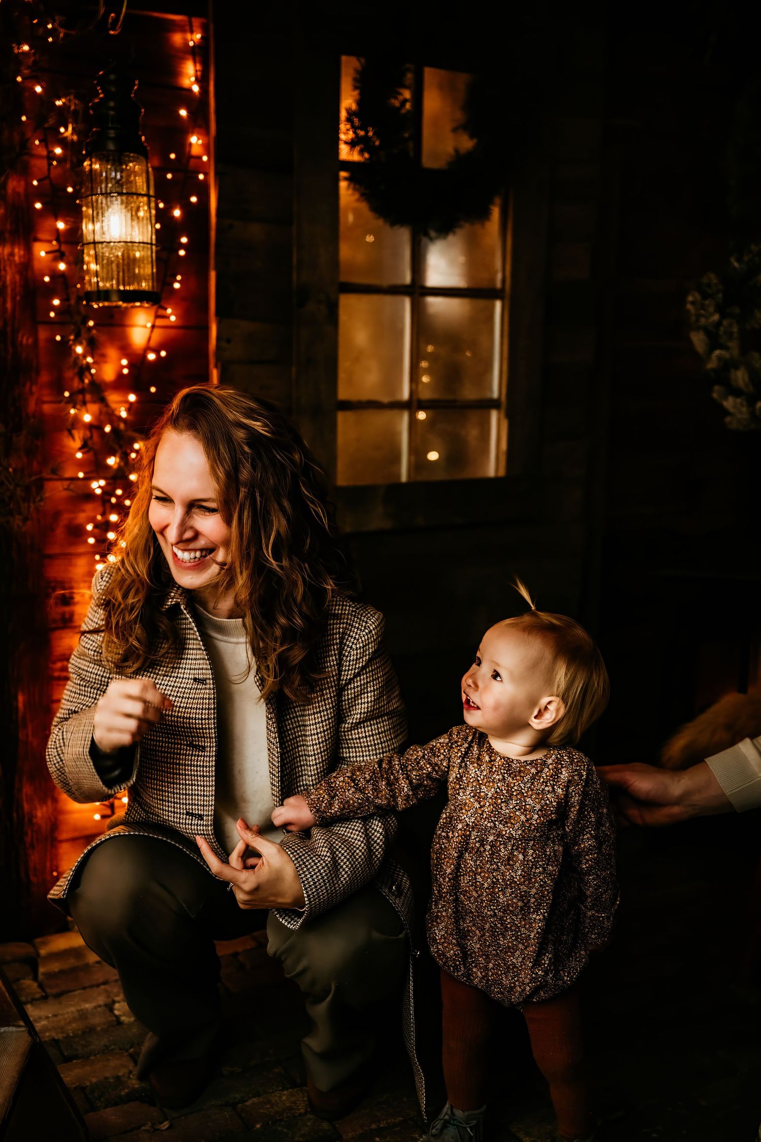 A parent and child share joyful moments together while sitting by twinkling holiday lights in a cozy evening setting.