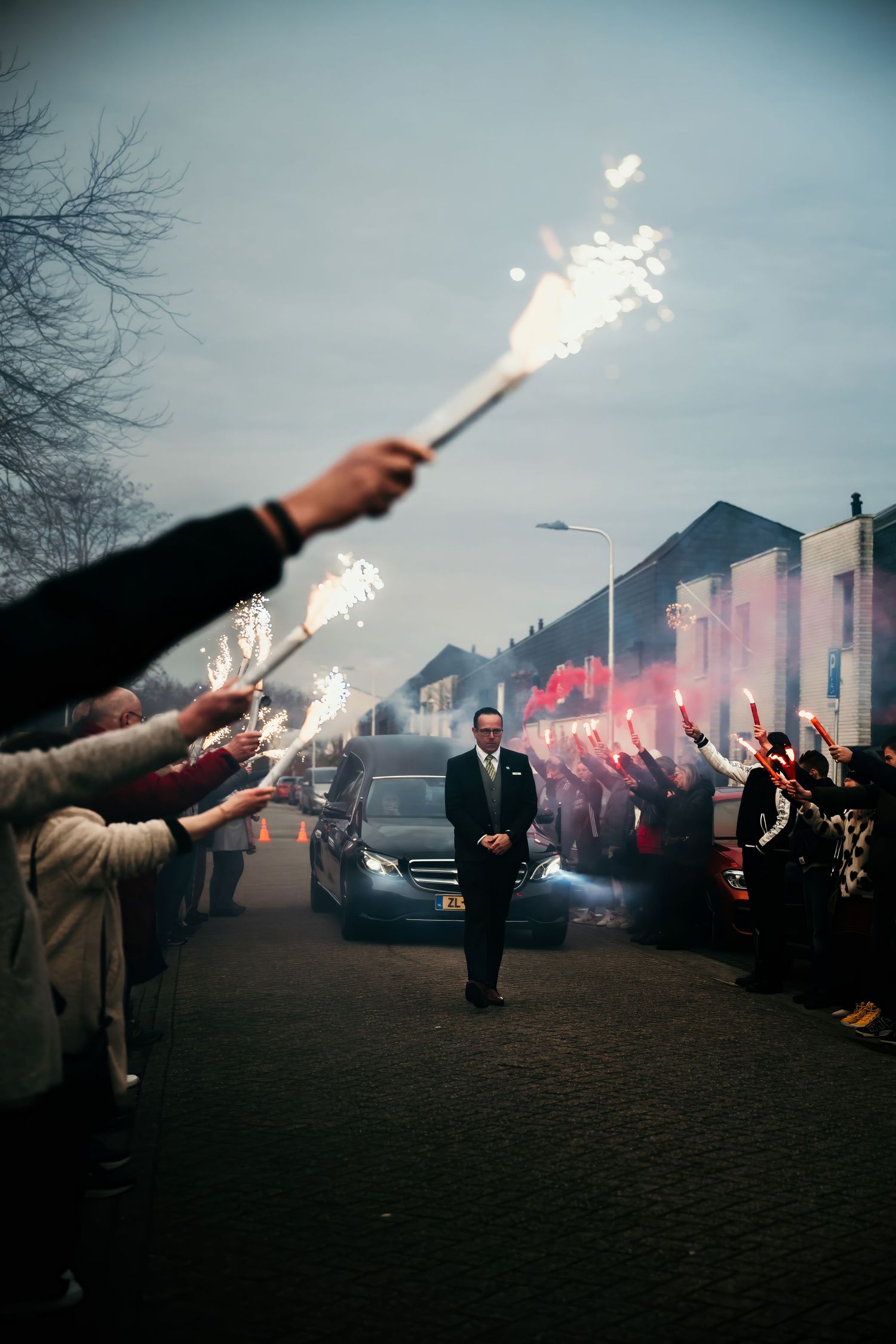 Silhouettes of people holding bright flares at dusk create a dramatic scene in an urban setting.