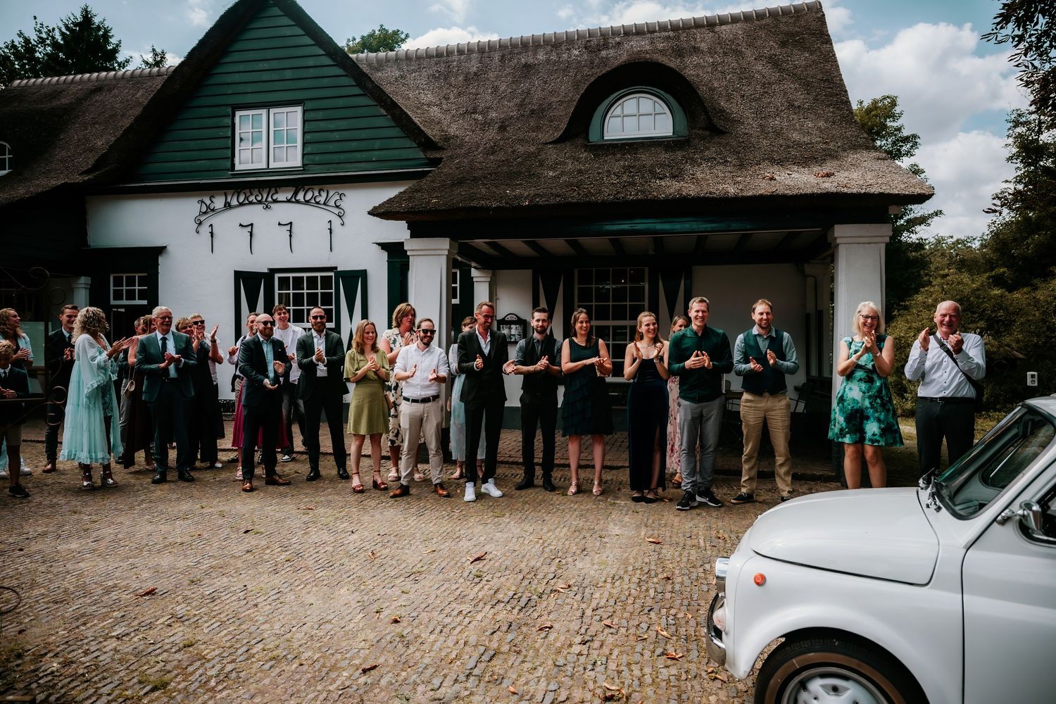 Wedding guests gathered outside a charming green and white cottage building.
