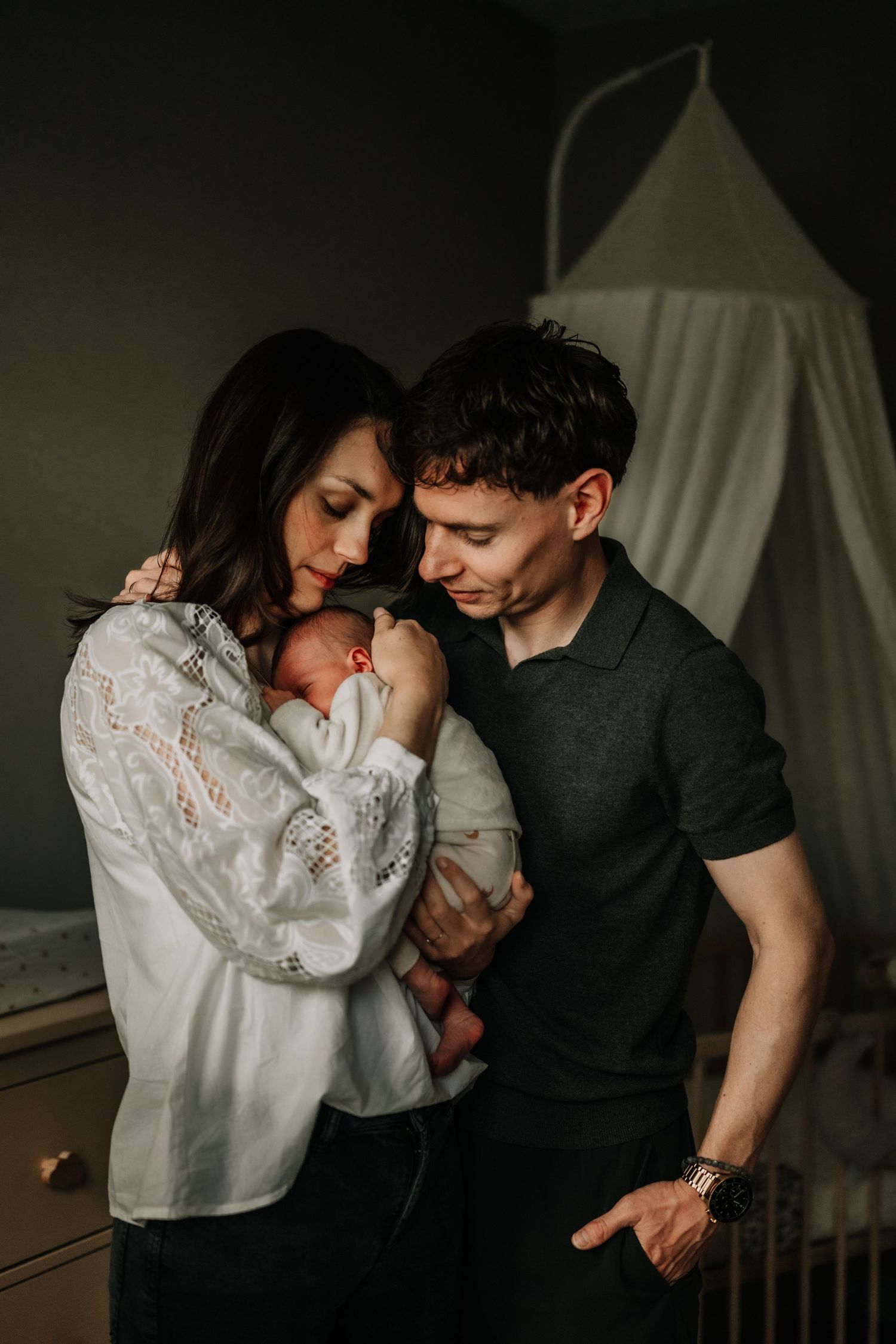A tender family moment near a white canopy in dim lighting.