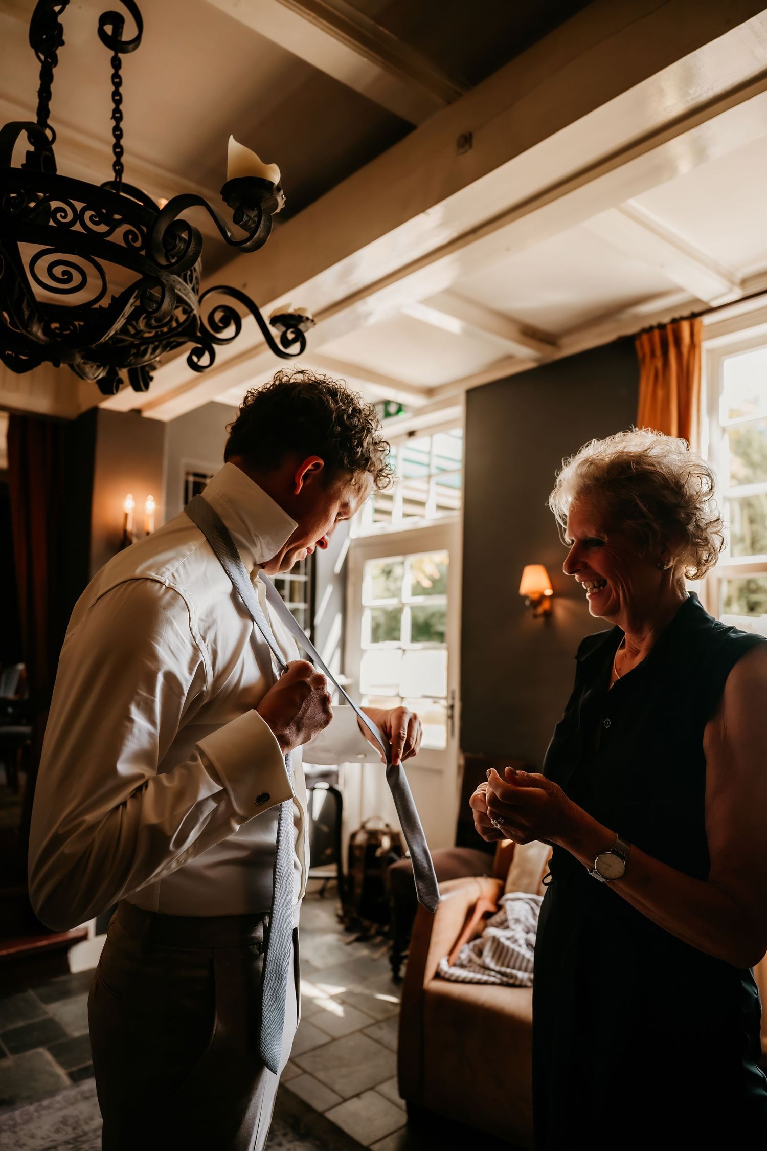 Warm indoor scene with ornate chandelier and two people conversing in elegant setting.