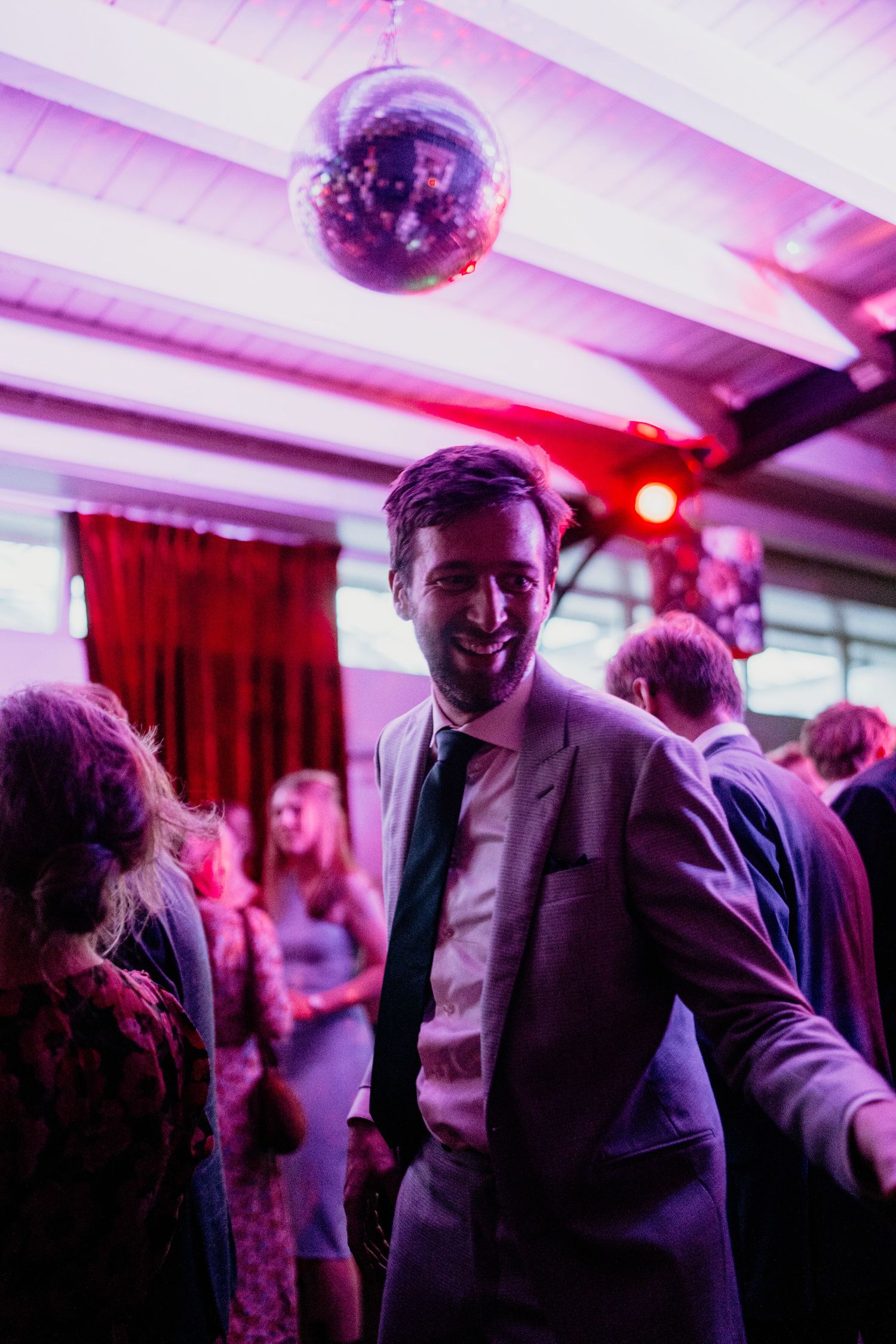 Wedding reception guests dance under purple and red lighting in a festive indoor venue.