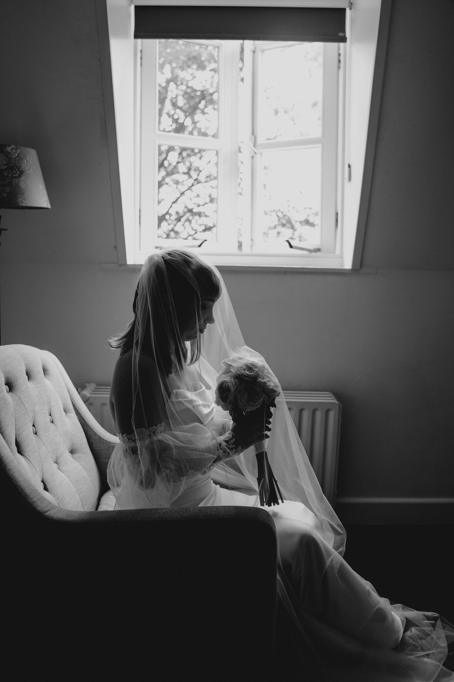 Silhouetted figure sitting by a bright window in a grey room with tufted furniture.