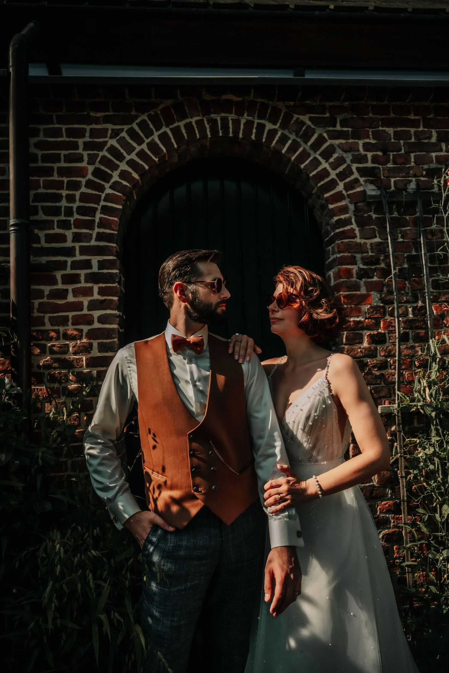 A romantic moment against a rustic brick wall with sunlight casting dramatic shadows.