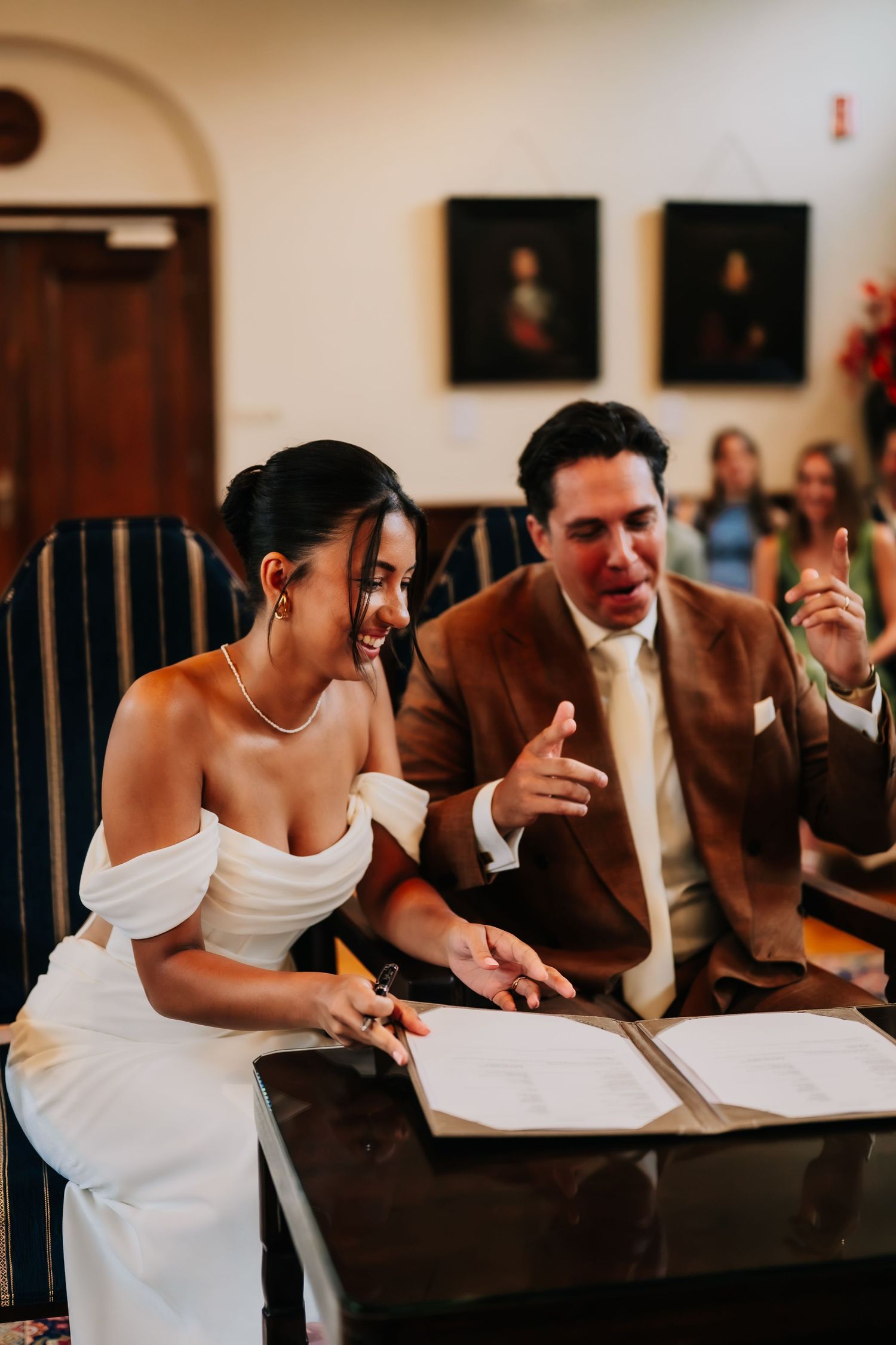 Bride and groom laughing together while signing wedding documents at a ceremony table.