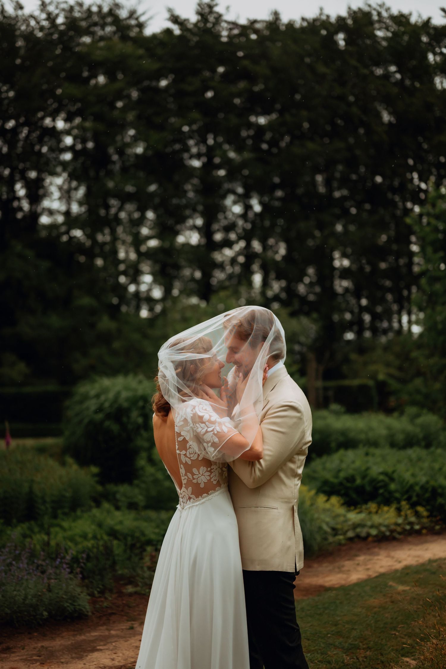 Bride and groom sharing a romantic kiss under a lace veil in a lush garden setting on their wedding day.