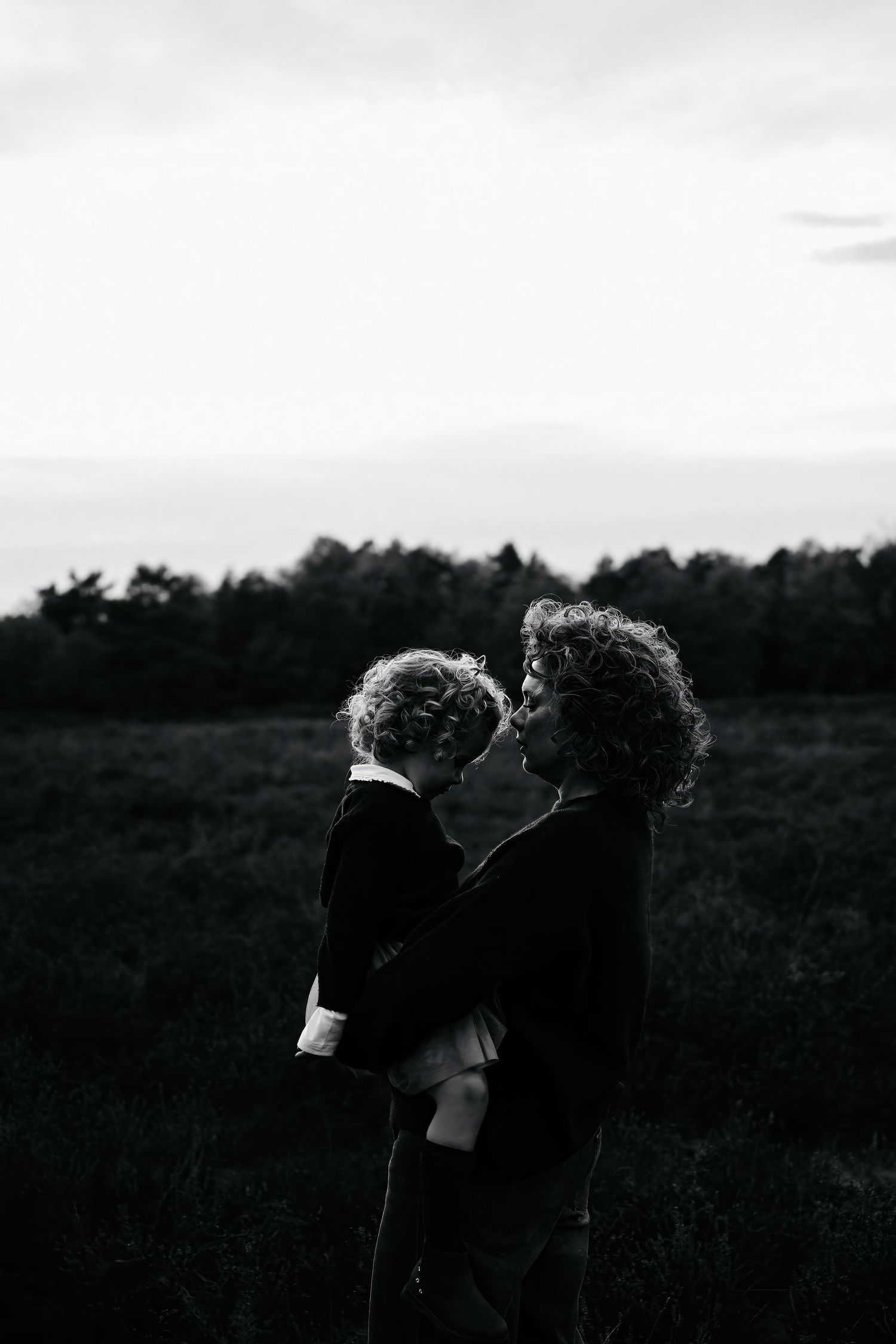 Silhouetted figures share an intimate moment against a moody grey sky.