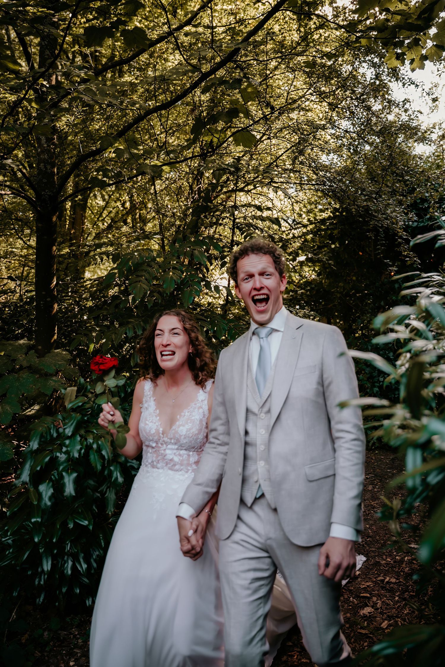 Joyful wedding couple laughing together in a lush garden setting.