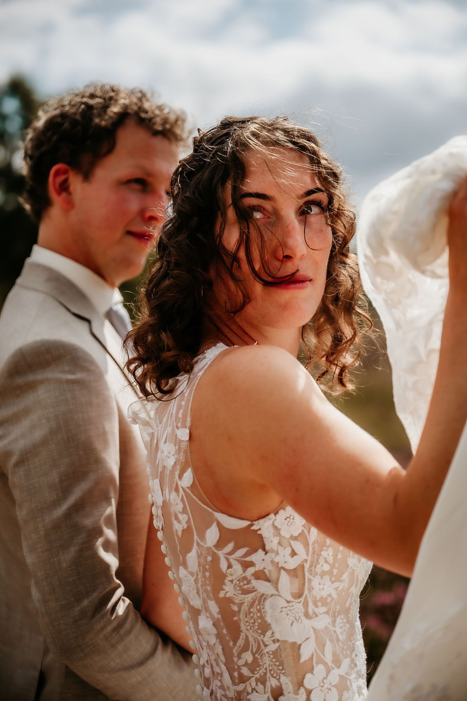 Wedding couple in elegant attire with lace details caught in natural sunlight.