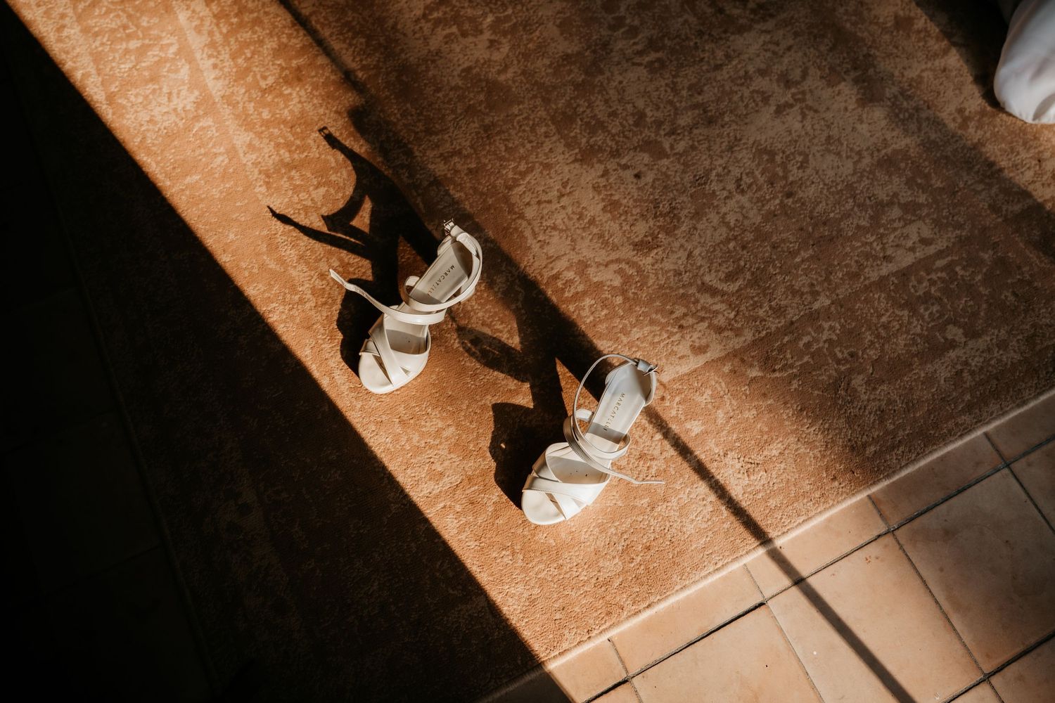 Dramatic shadow of wedding shoes cast on terracotta tiles in sunlight.
