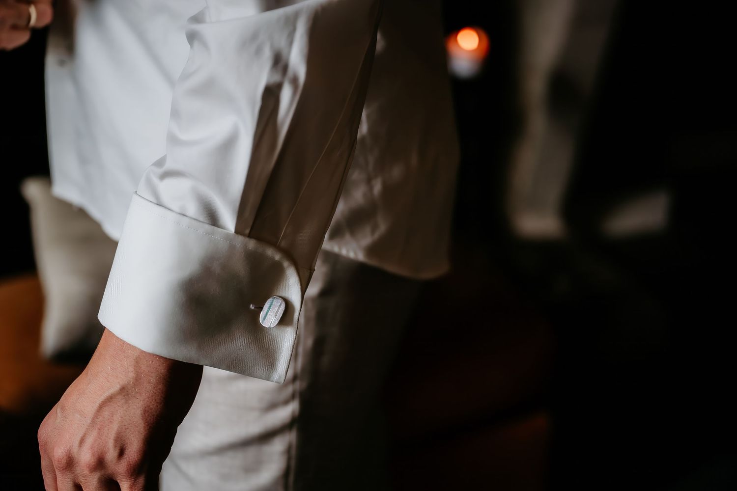 Close-up detail of a white chef coat sleeve with cufflinks in a dimly lit setting.