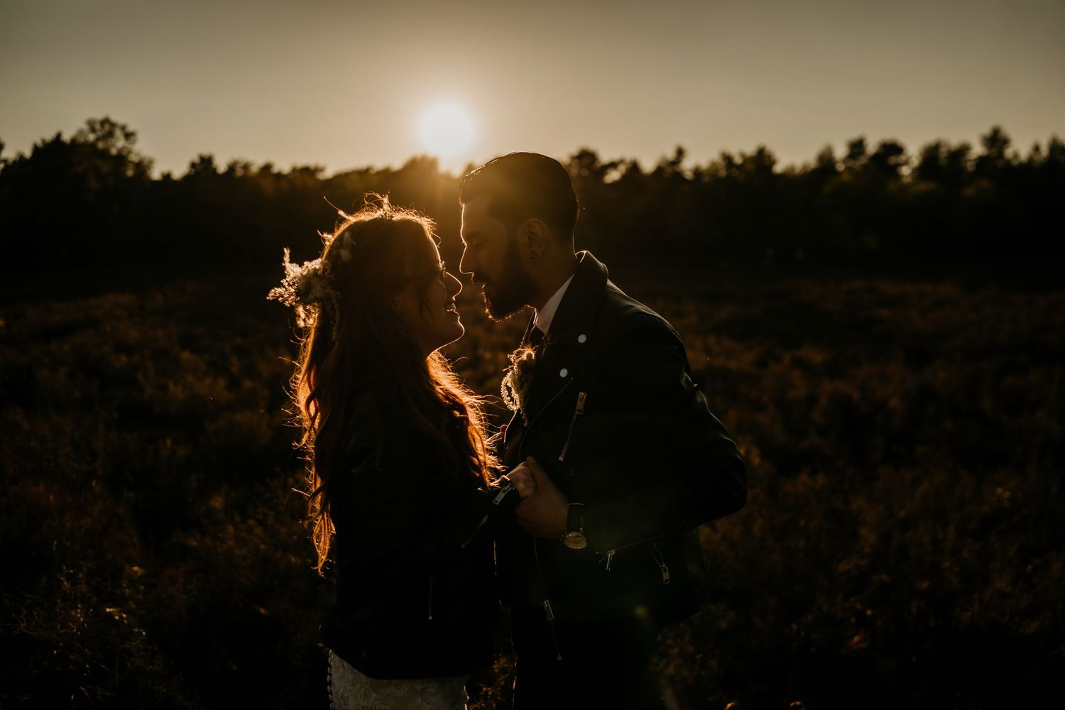 Silhouetted couple embracing in a golden sunset field.