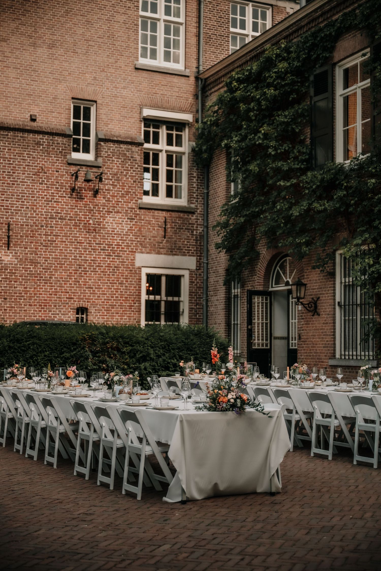 Outdoor wedding reception setup with white chairs and tables in front of a brick building.
