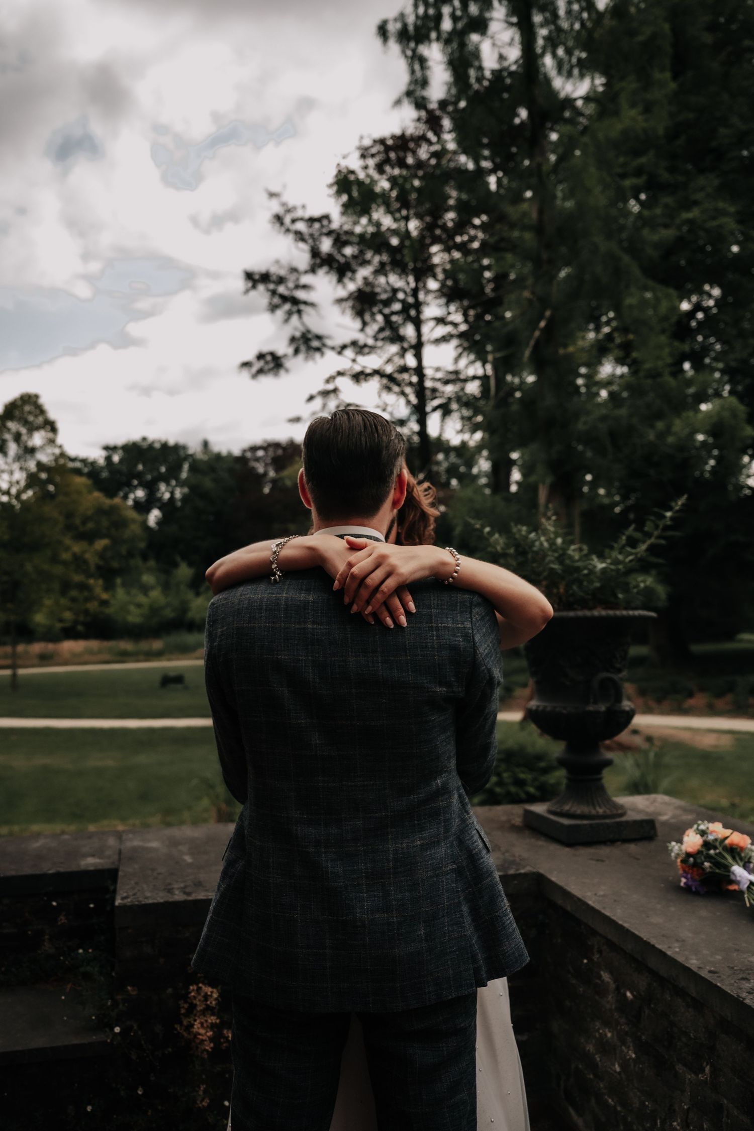 Couple embracing outdoors against a cloudy sky with trees in the background.