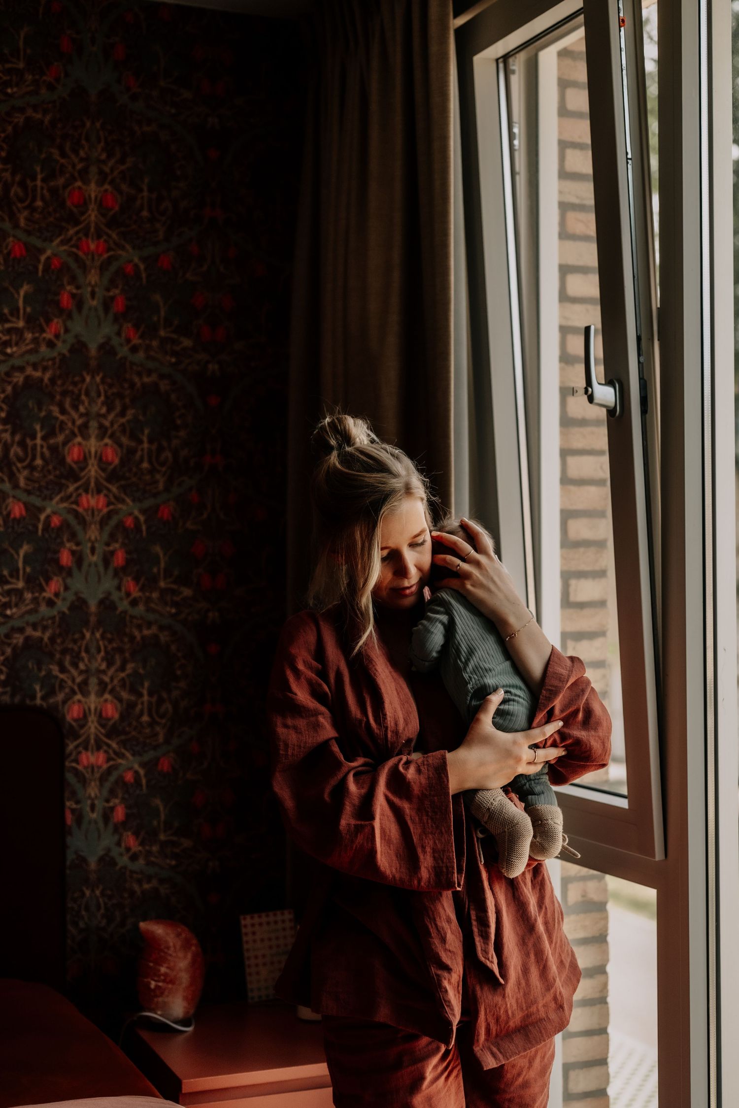 Peaceful moment by a window with ornate red wallpaper and natural light.