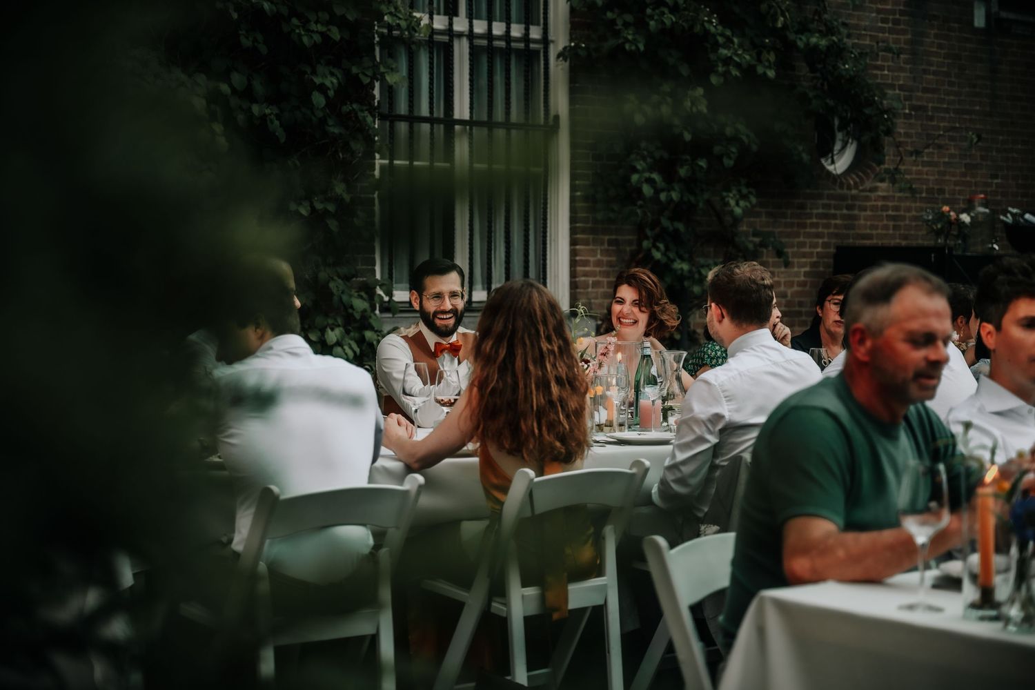 Outdoor wedding reception with tables set among greenery and brick walls.