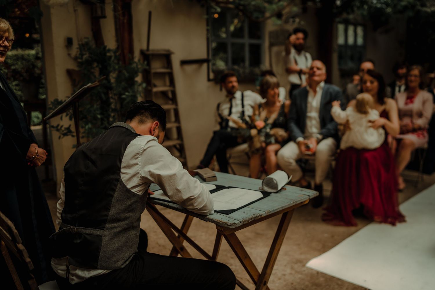 A musician performs at a rustic outdoor wedding ceremony with guests seated in the background.