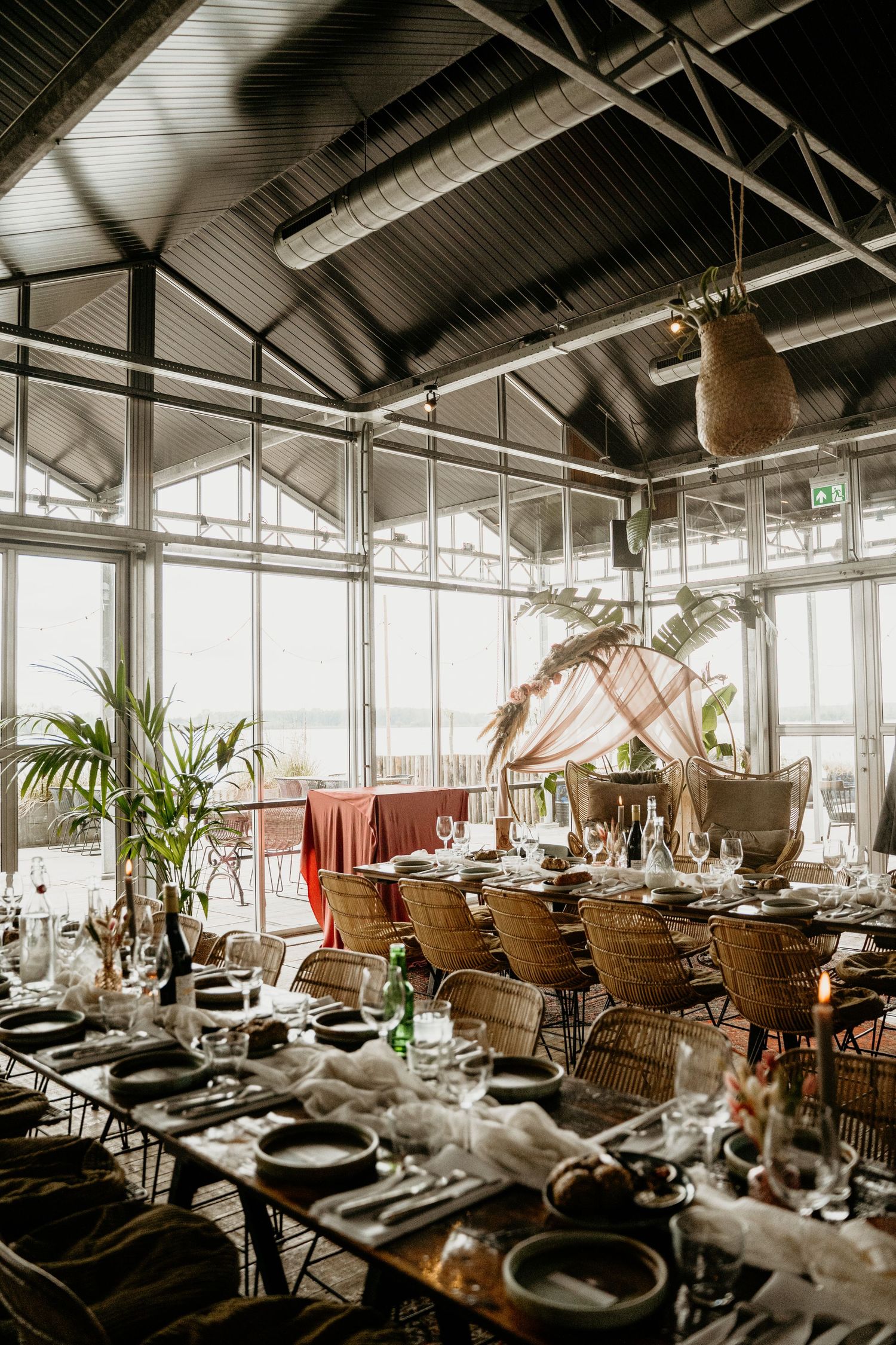 An elegant wedding reception venue with rattan chairs and table settings under a vaulted glass ceiling.