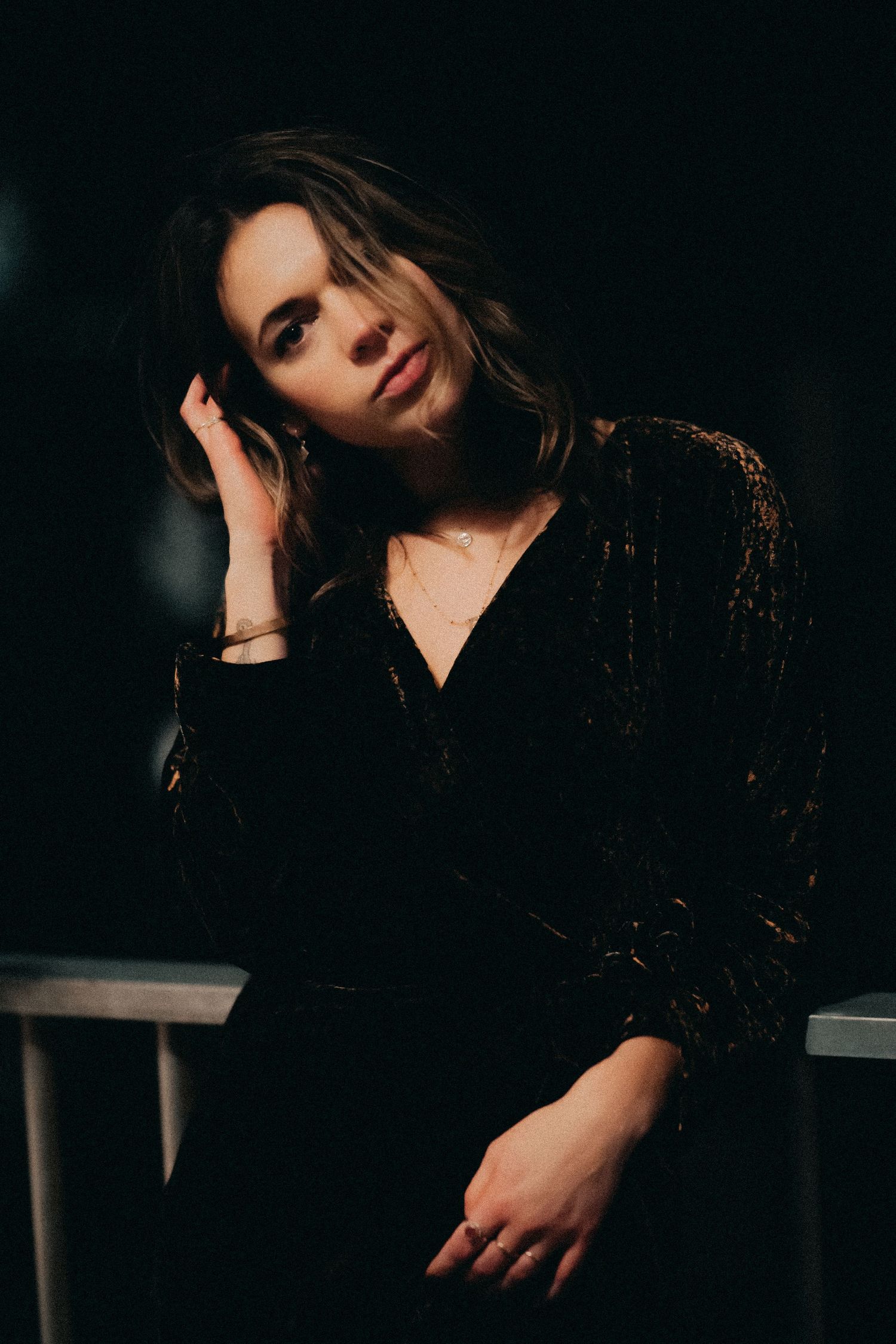 Dramatic moody portraits in dark lighting show a figure in black clothing posing against shadowy background.