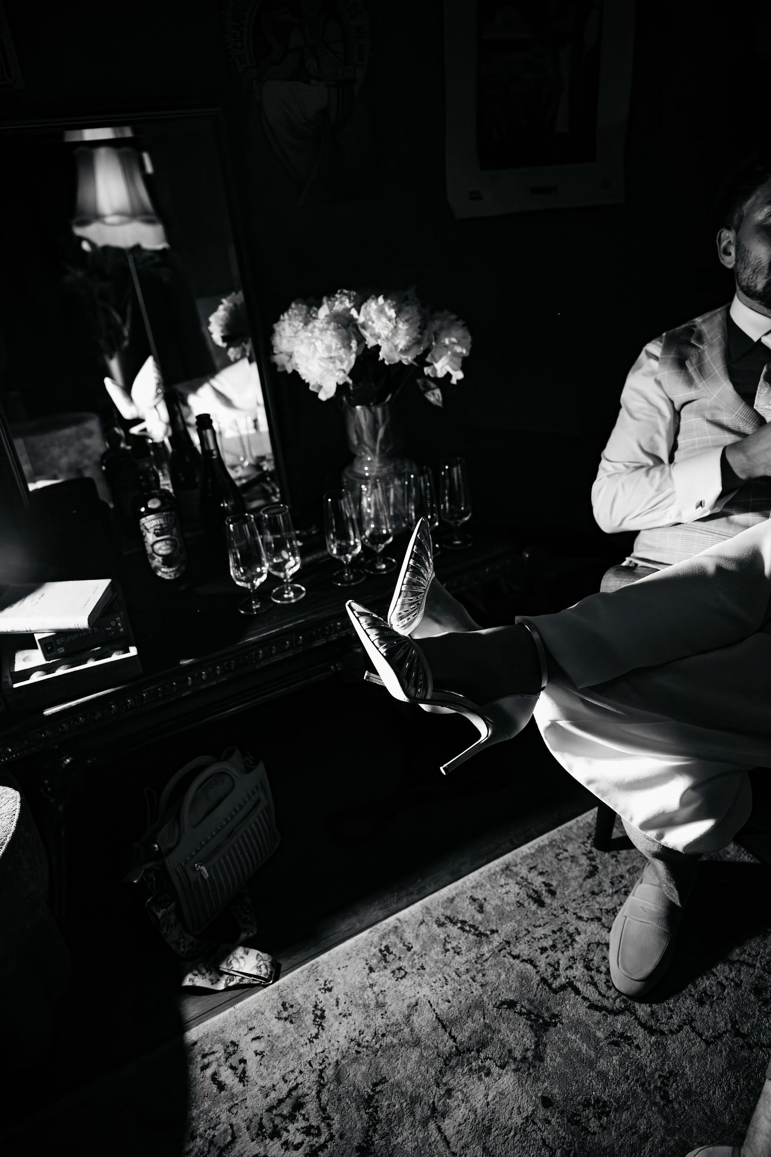 Black and white photo of a man in a suit sitting beside a table with flowers and glassware in an elegant room.