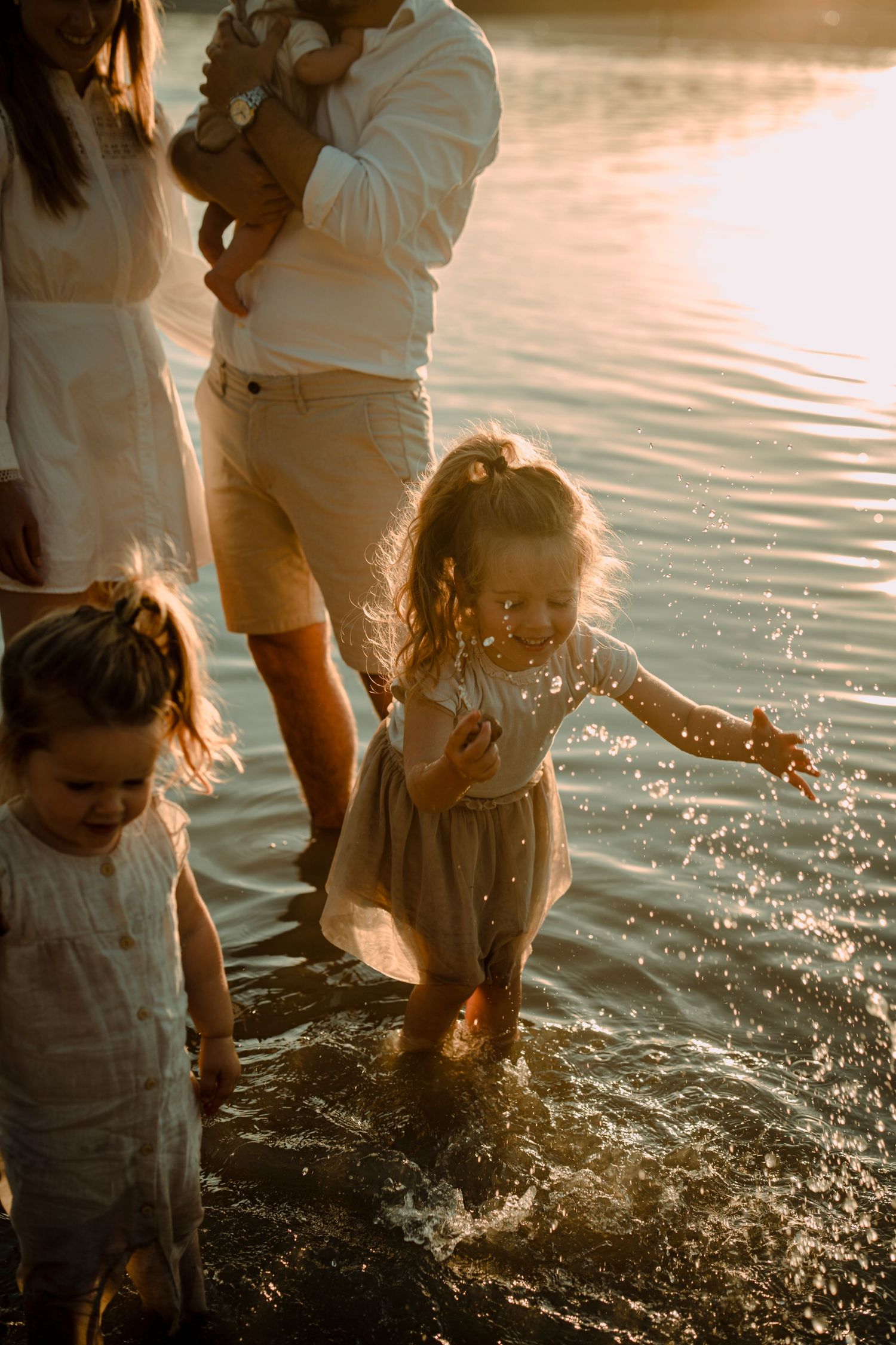 Children playing and splashing in glowing water at sunset while wearing light colored clothing.