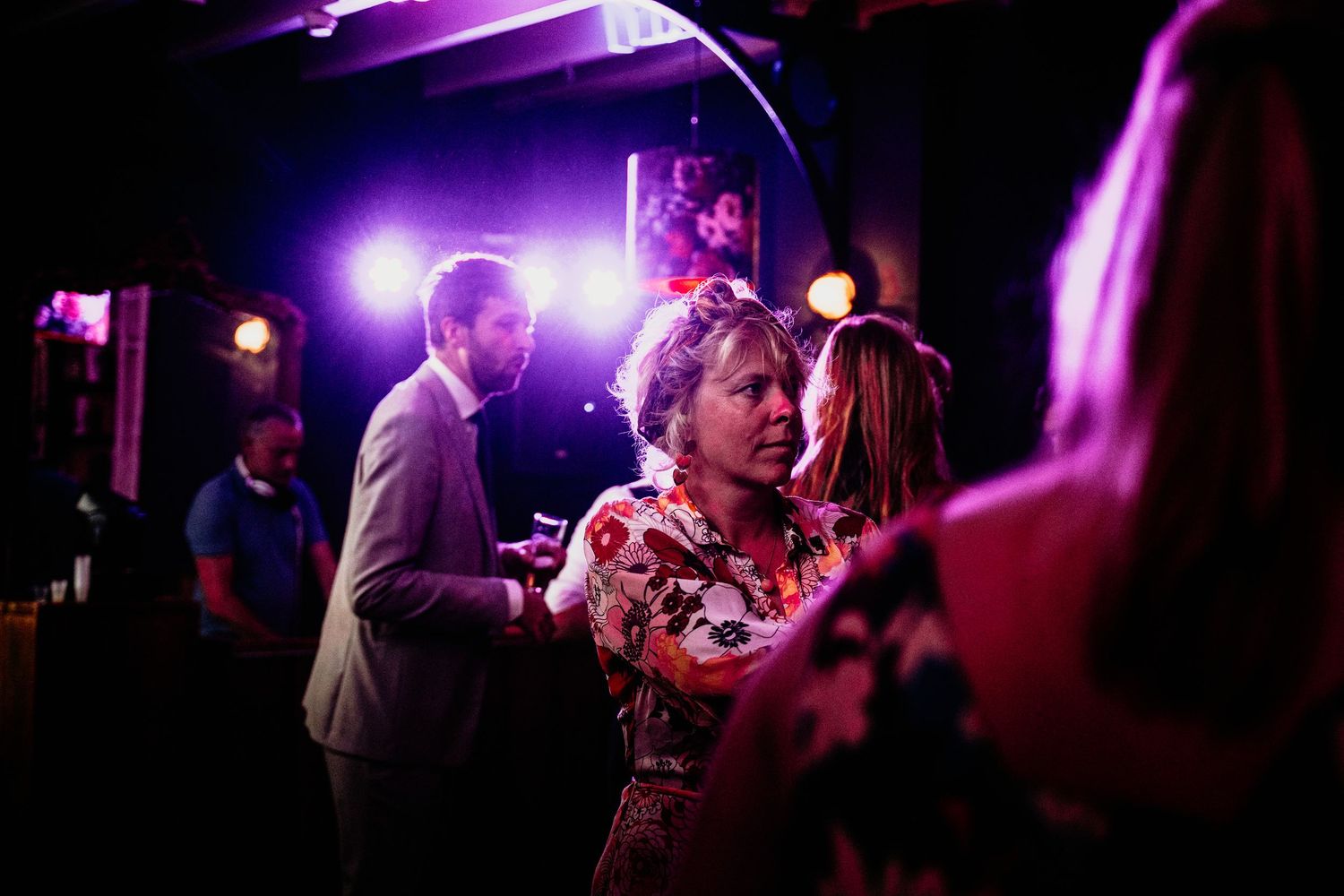 Wedding guests dance under dramatic purple lighting at a reception party with a vibrant nightclub atmosphere.