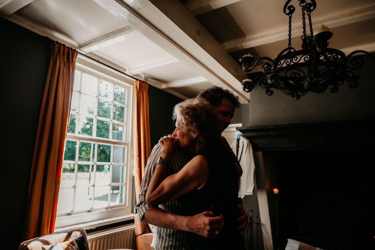 A romantic couple shares an intimate moment in a sunlit room with orange curtains and wooden beams.