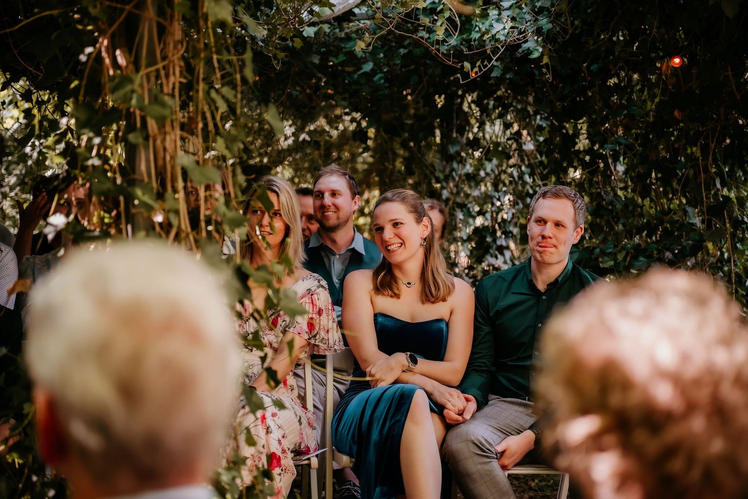 Wedding guests seated outdoors under natural greenery during a garden ceremony.