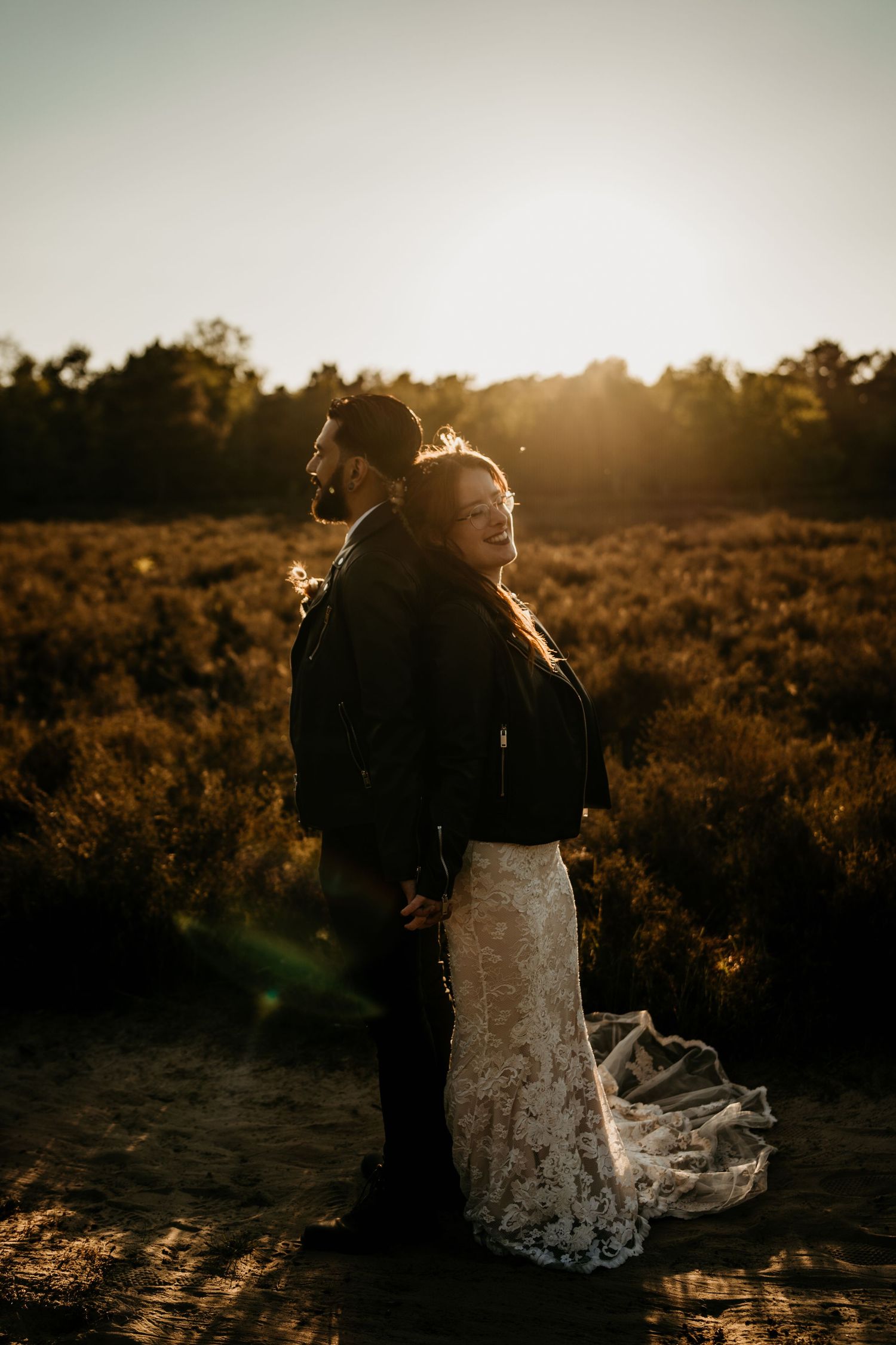 Silhouetted couple embracing in golden sunset light with flowing lace wedding dress.