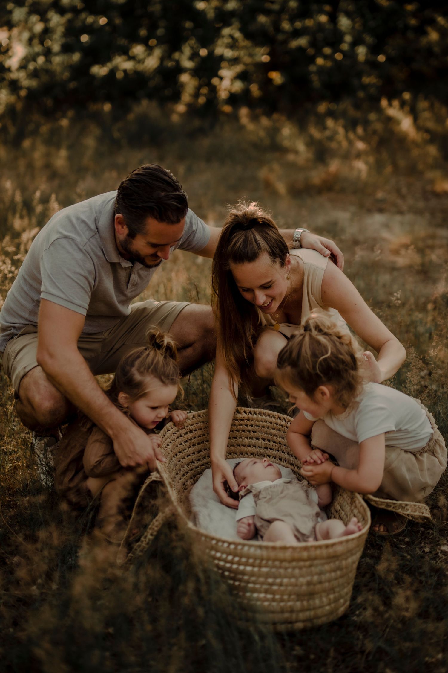 A family gathers around a woven basket in a sun-dappled outdoor setting.