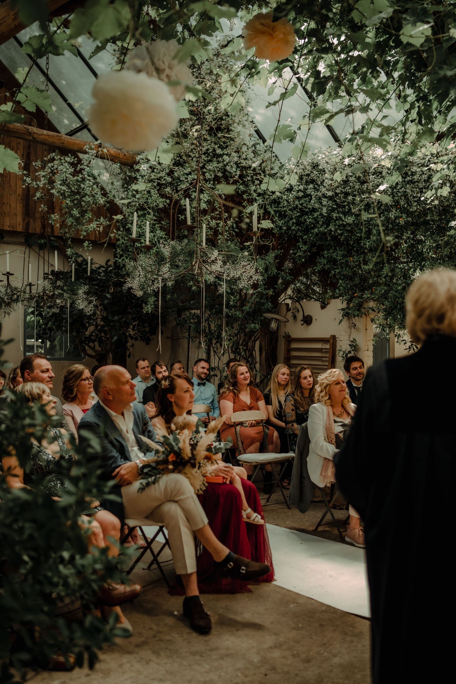 Intimate garden wedding ceremony with guests seated among lush greenery and paper lantern decorations.