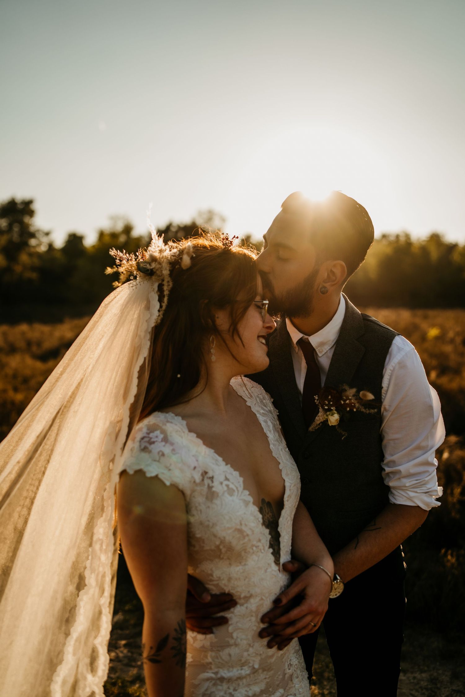 A backlit wedding couple sharing an intimate moment in a field during golden hour.