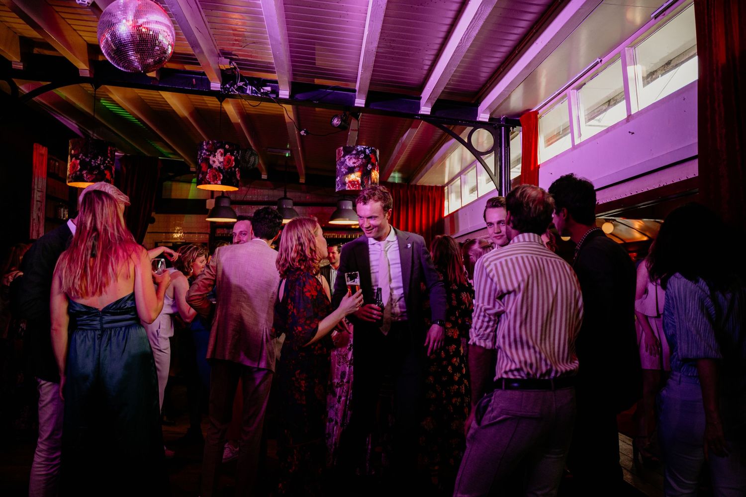 People dancing and socializing under purple lighting at a nightclub event.